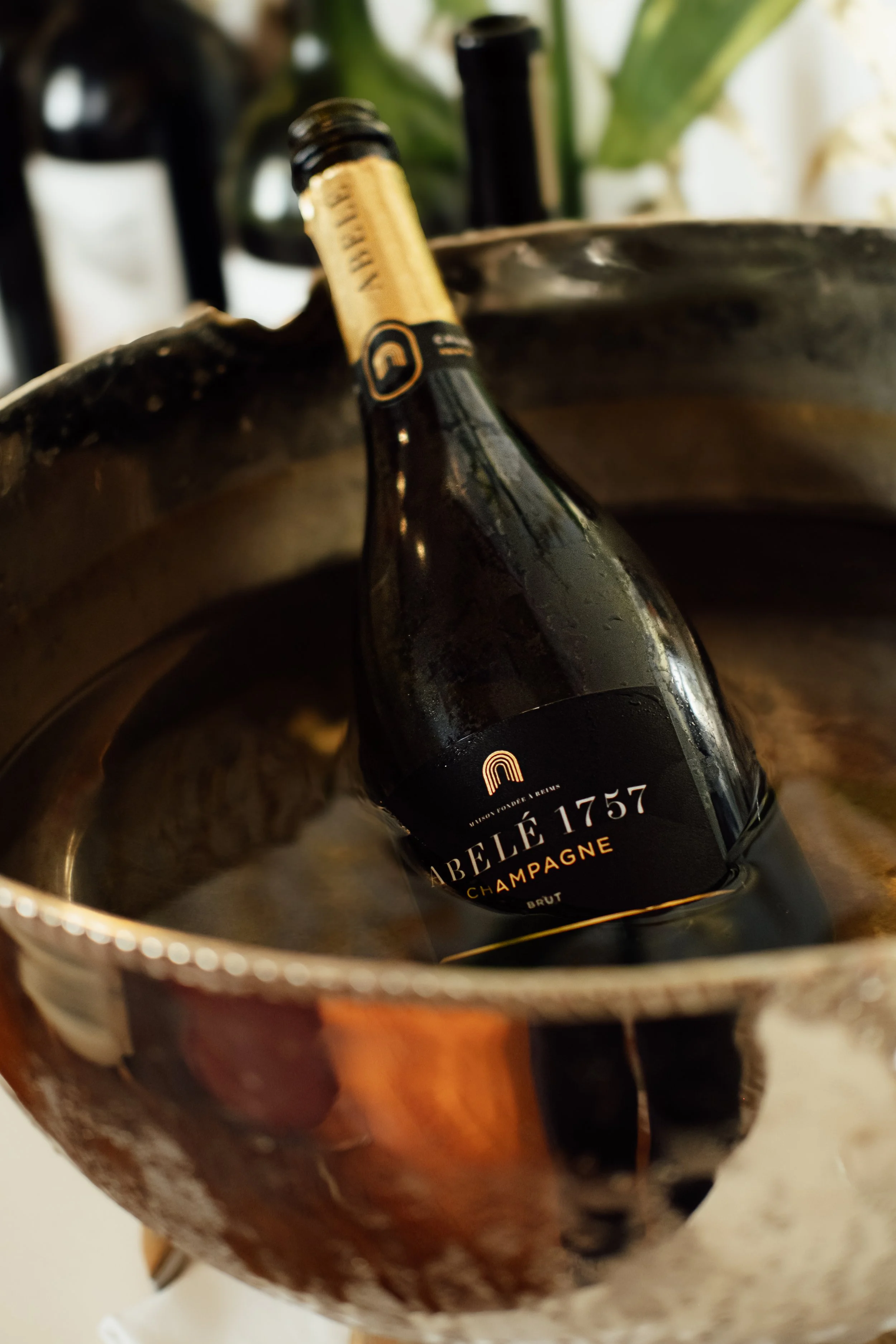 A bottle of Champagne inside a bronze-colored ice bucket.