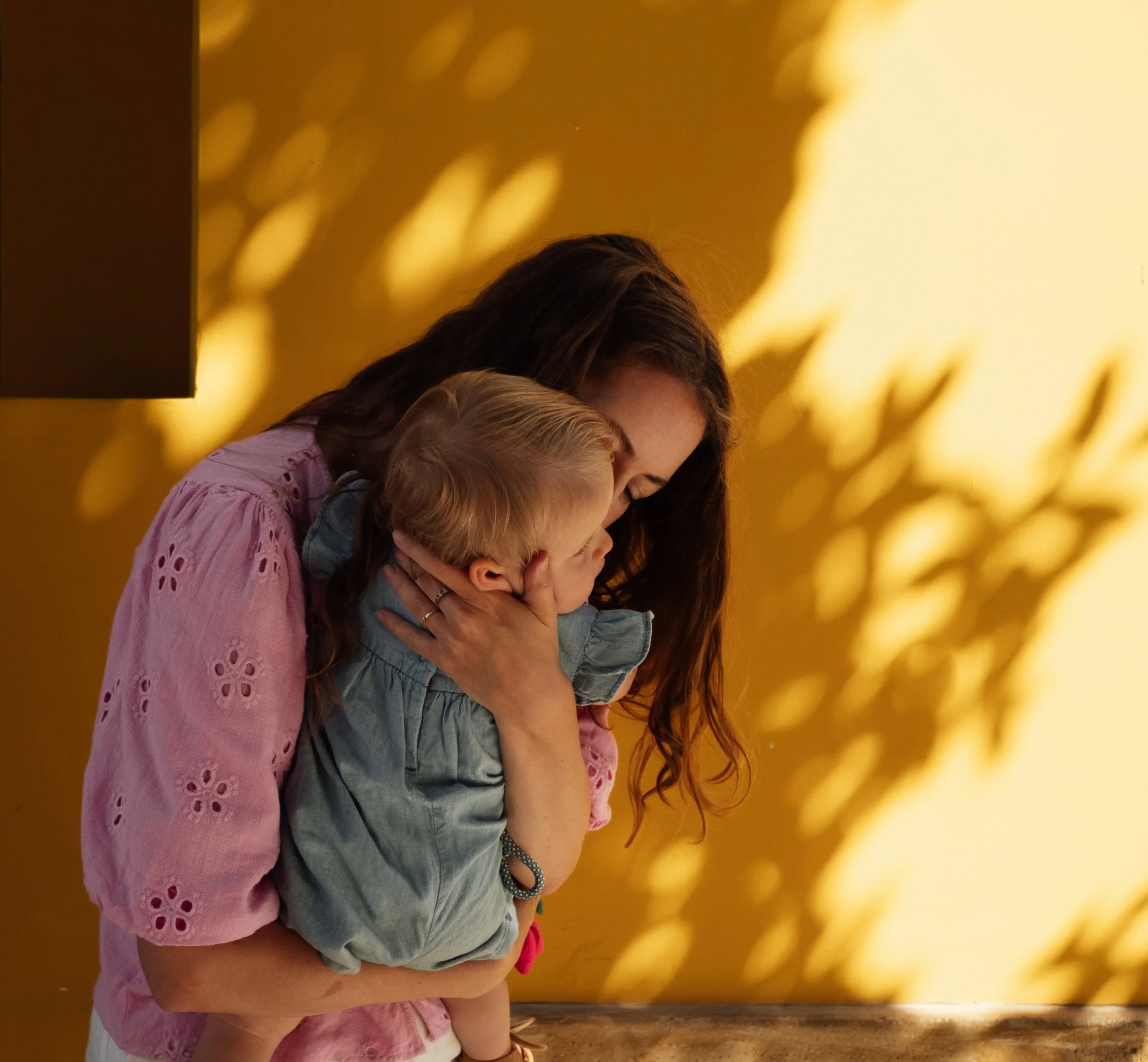 Three girls leaning their heads together, beautiful yellow wall with shadows in the background.