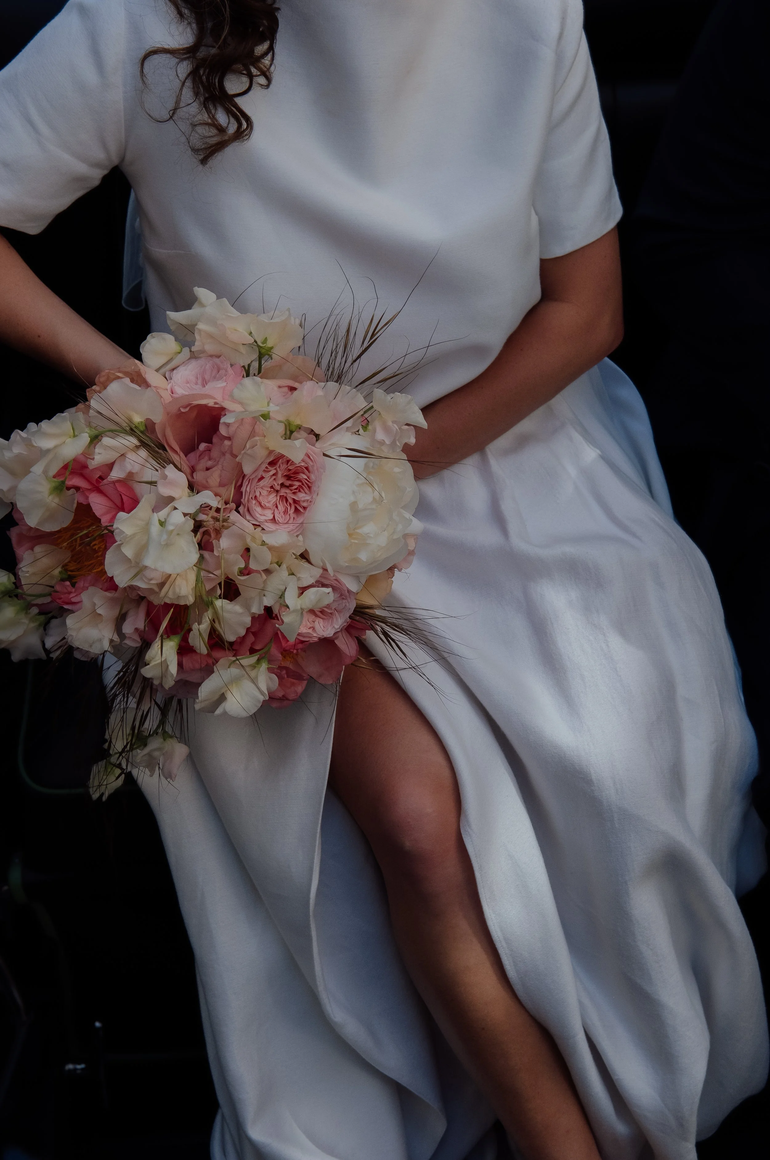 A woman in a white dress holding a bouquet of pink and white flowers, with long curly hair.
