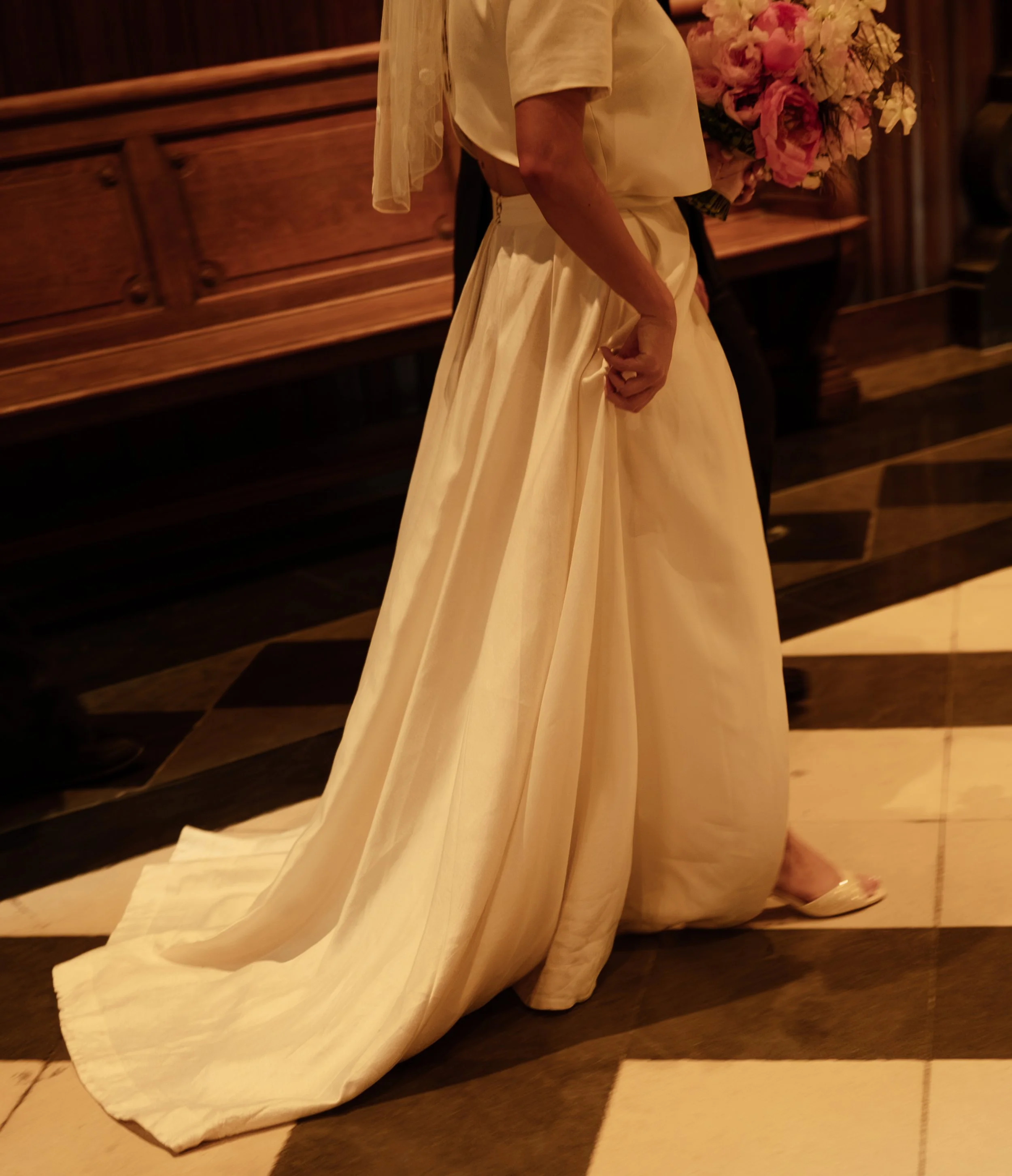 A person holding a large bouquet of pink and white flowers during a formal event, standing on a polished wooden floor with a wood-paneled background.