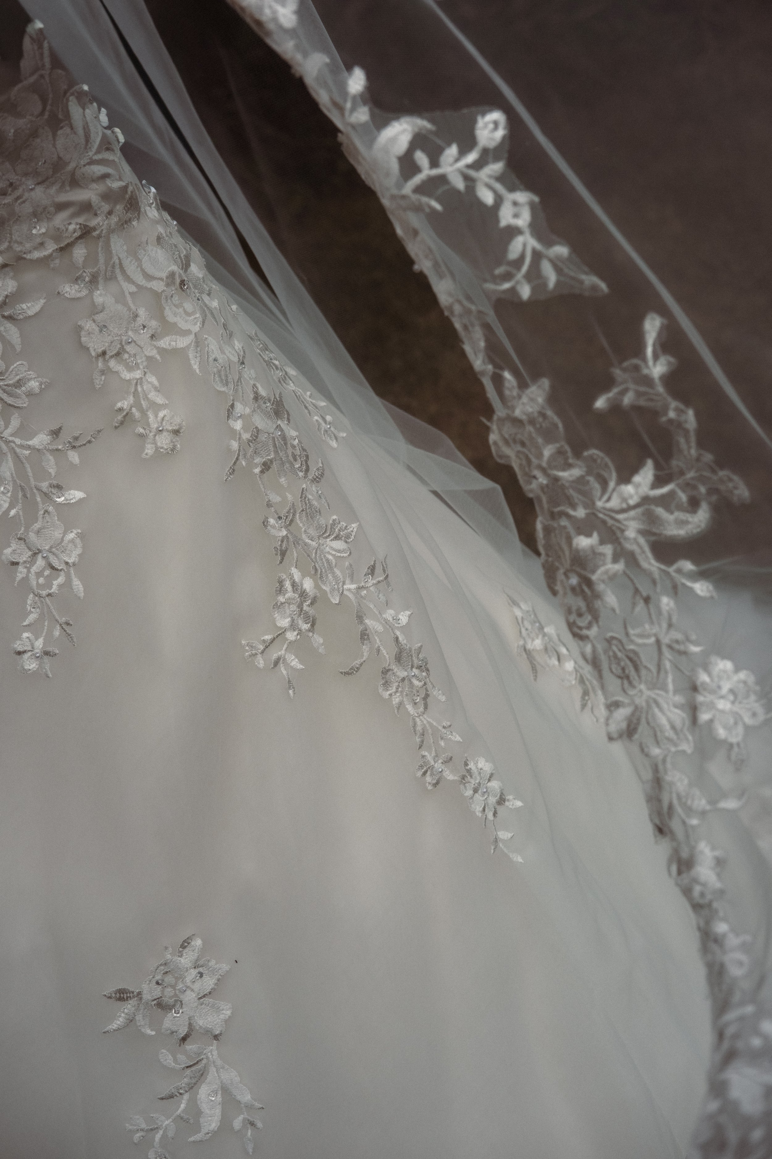 Close-up of a section of white lace fabric with floral embroidery and small beads, part of a wedding dress or similar garment.