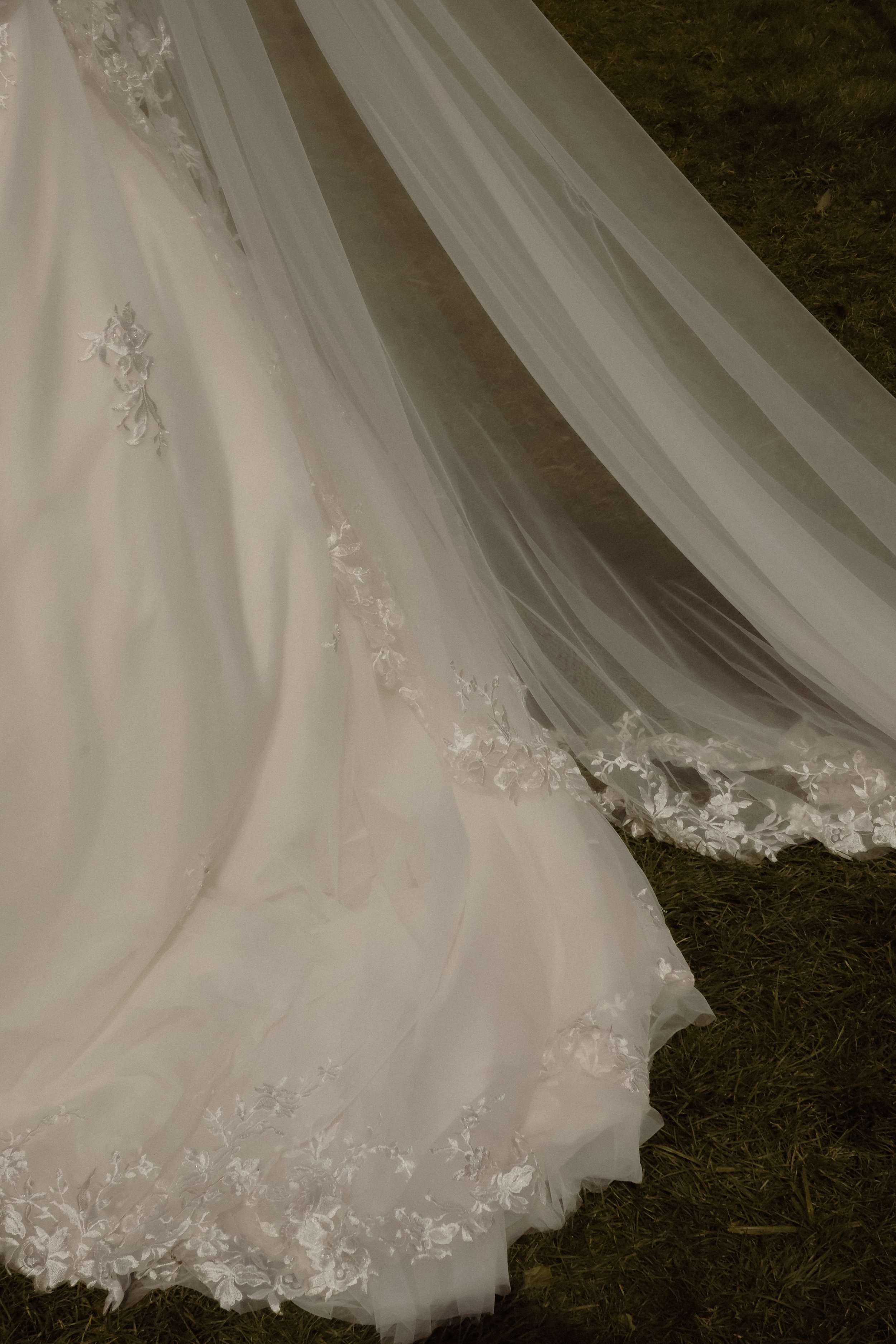 Close-up of a white wedding dress with lace and embroidery, lying on grass.