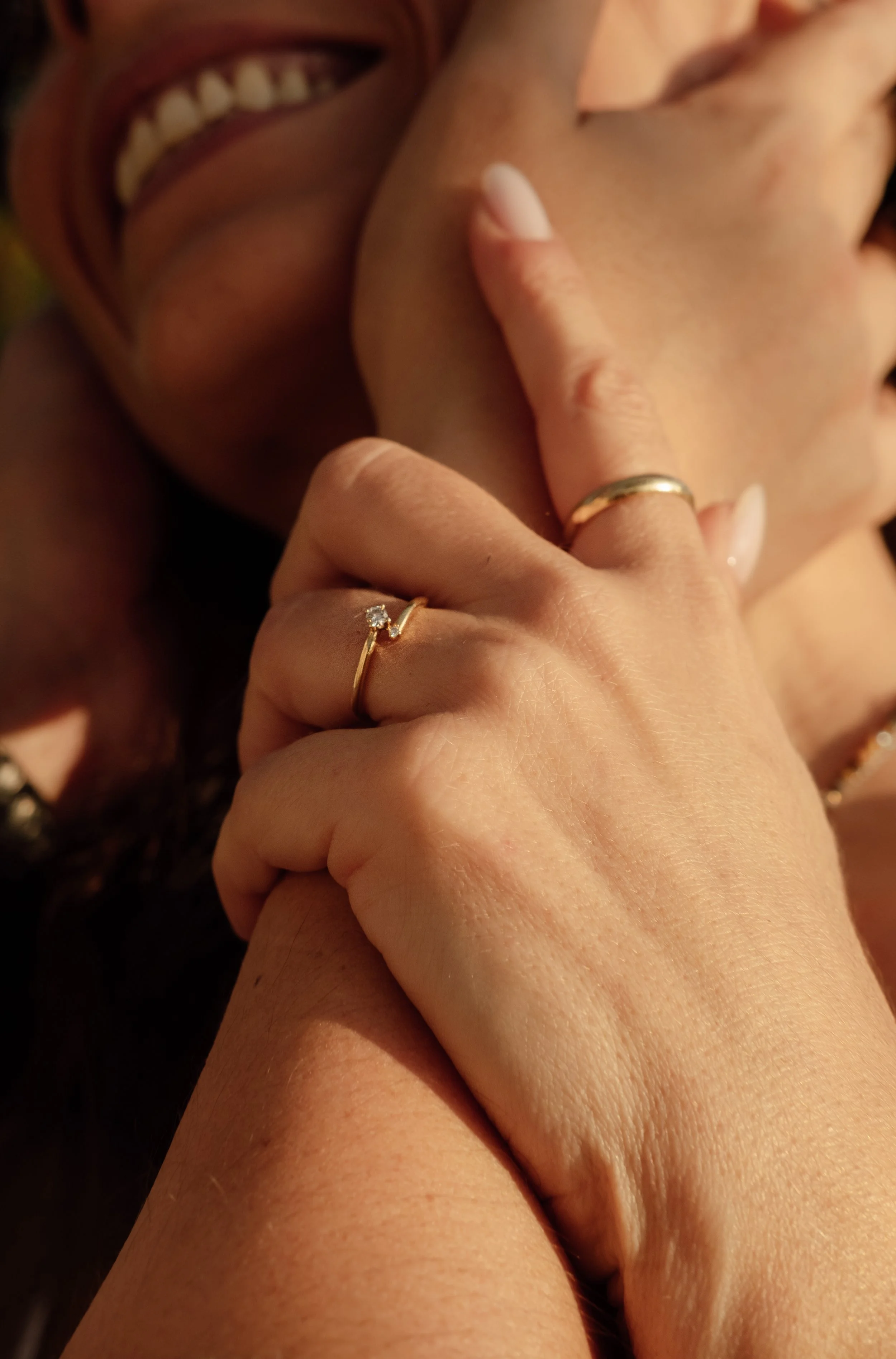 Close-up of a person smiling and touching their face, wearing rings on fingers, with warm lighting.