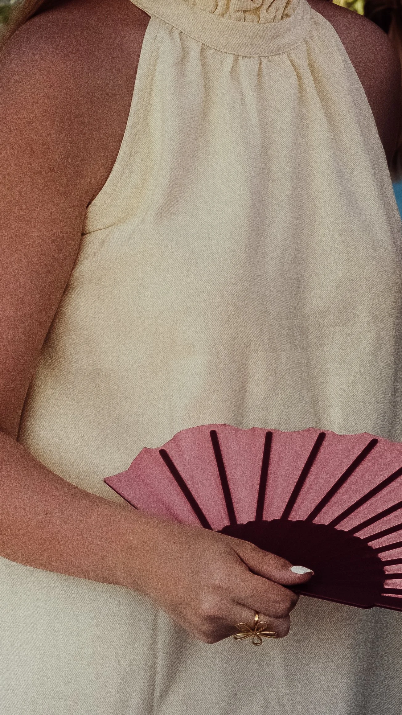 Close-up of a person wearing a cream-colored dress, holding a pink and black fan.