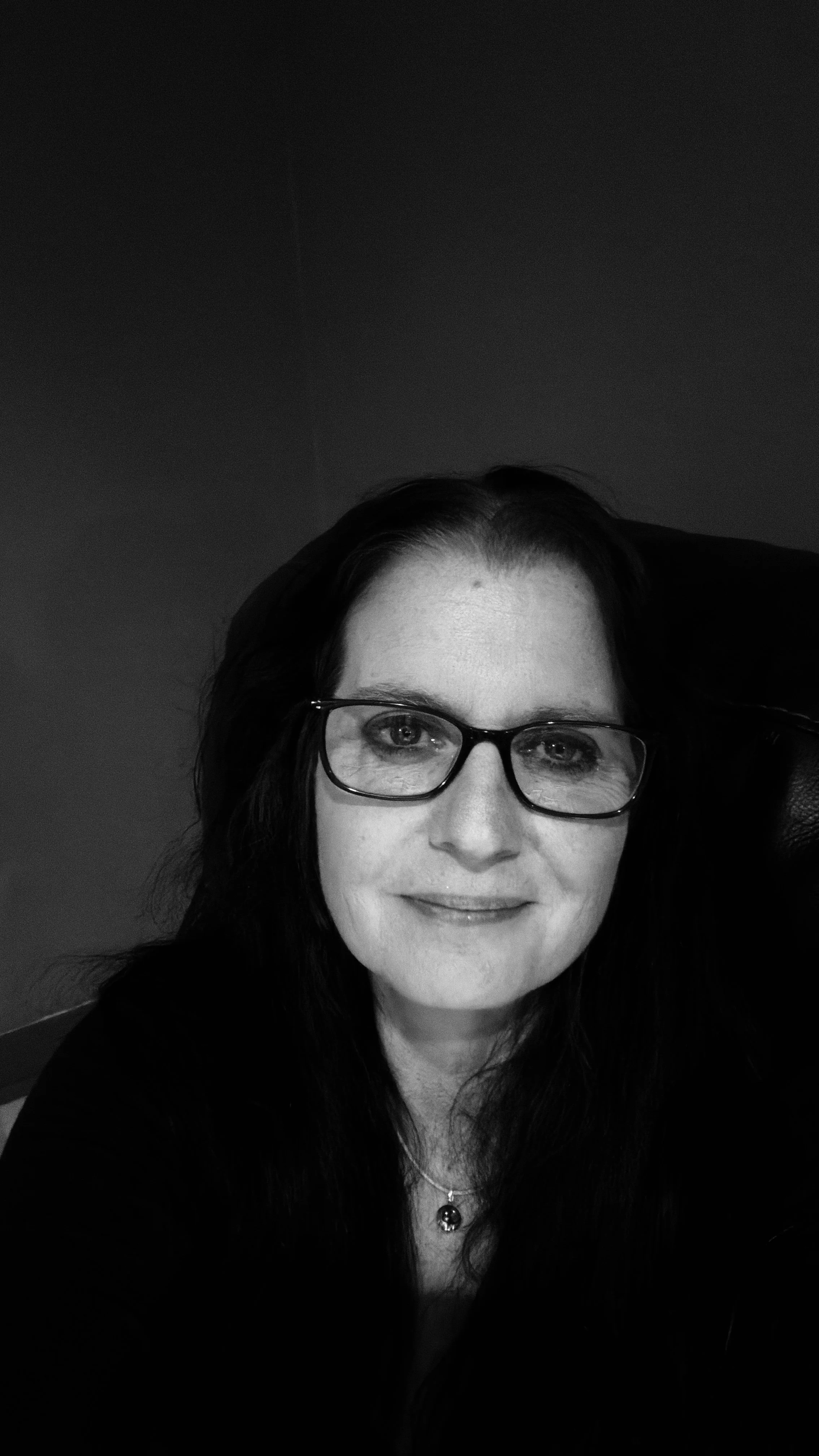 A woman with long dark hair and glasses smiling at the camera in black and white.