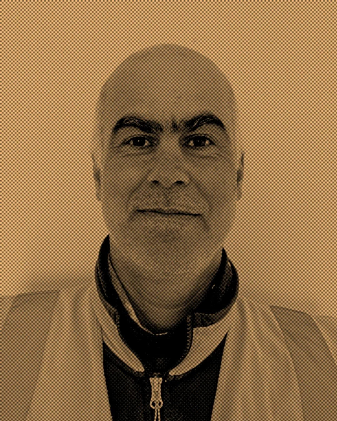 Close-up of a man with short dark hair, wearing a jacket with a zipper, facing the camera with a neutral expression.