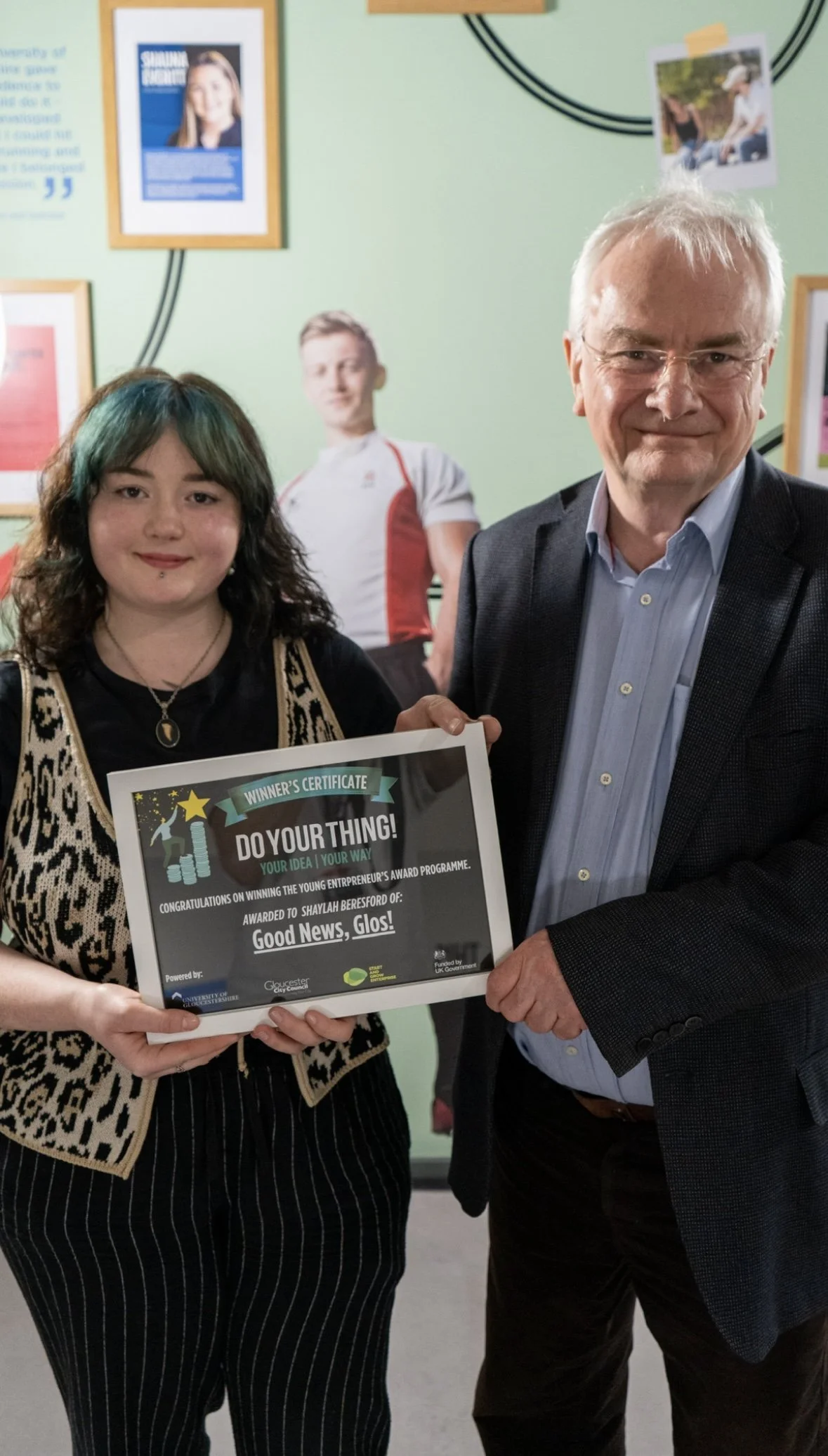 Good News, Glos! Founder Shaylah Beresford and Jeremy Hilton, Leader of the council, holding a certificate together at the University of Gloucestershire.