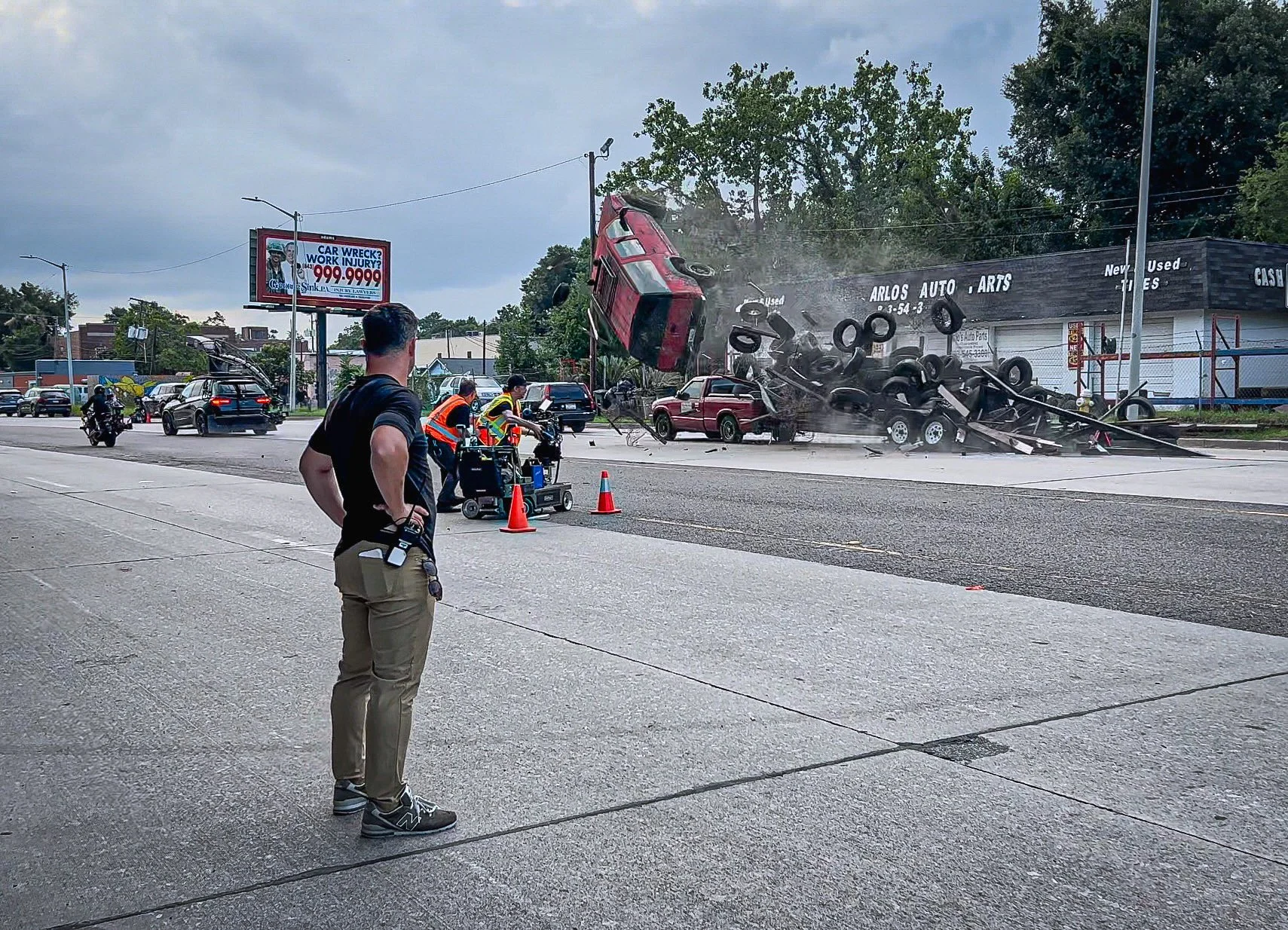 A red SUV crashed into a building, causing severe damage and debris. Emergency response teams are on the scene, and a person is standing nearby observing the situation.
