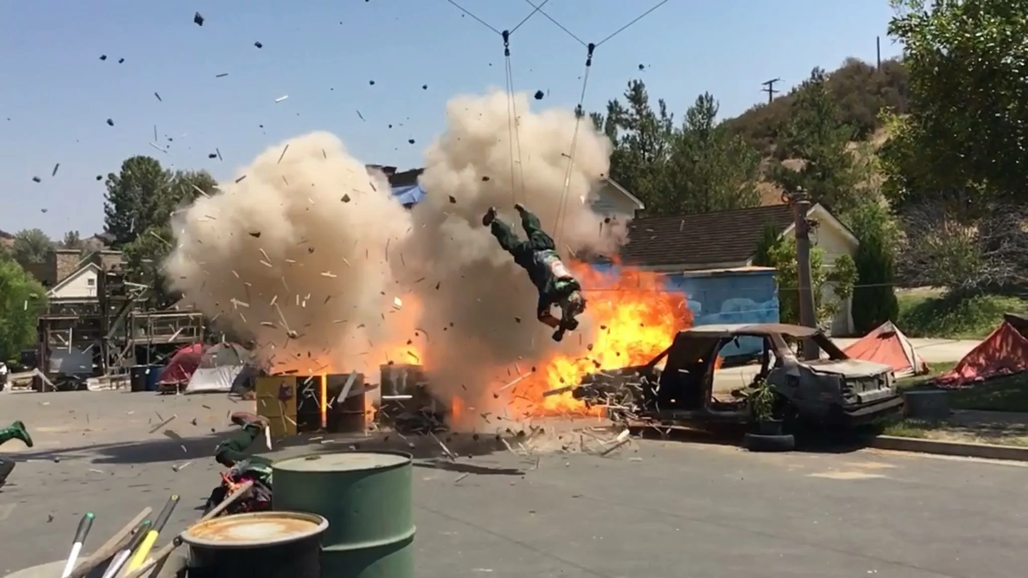 Explosion in a backyard with a fireball, smoke, debris, and a person flying through the air upside down.