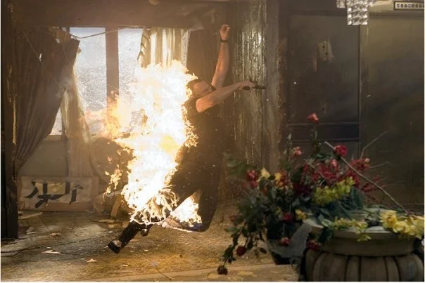 A person running away from a large fire and explosion in an indoor setting, with debris and smoke in the background.