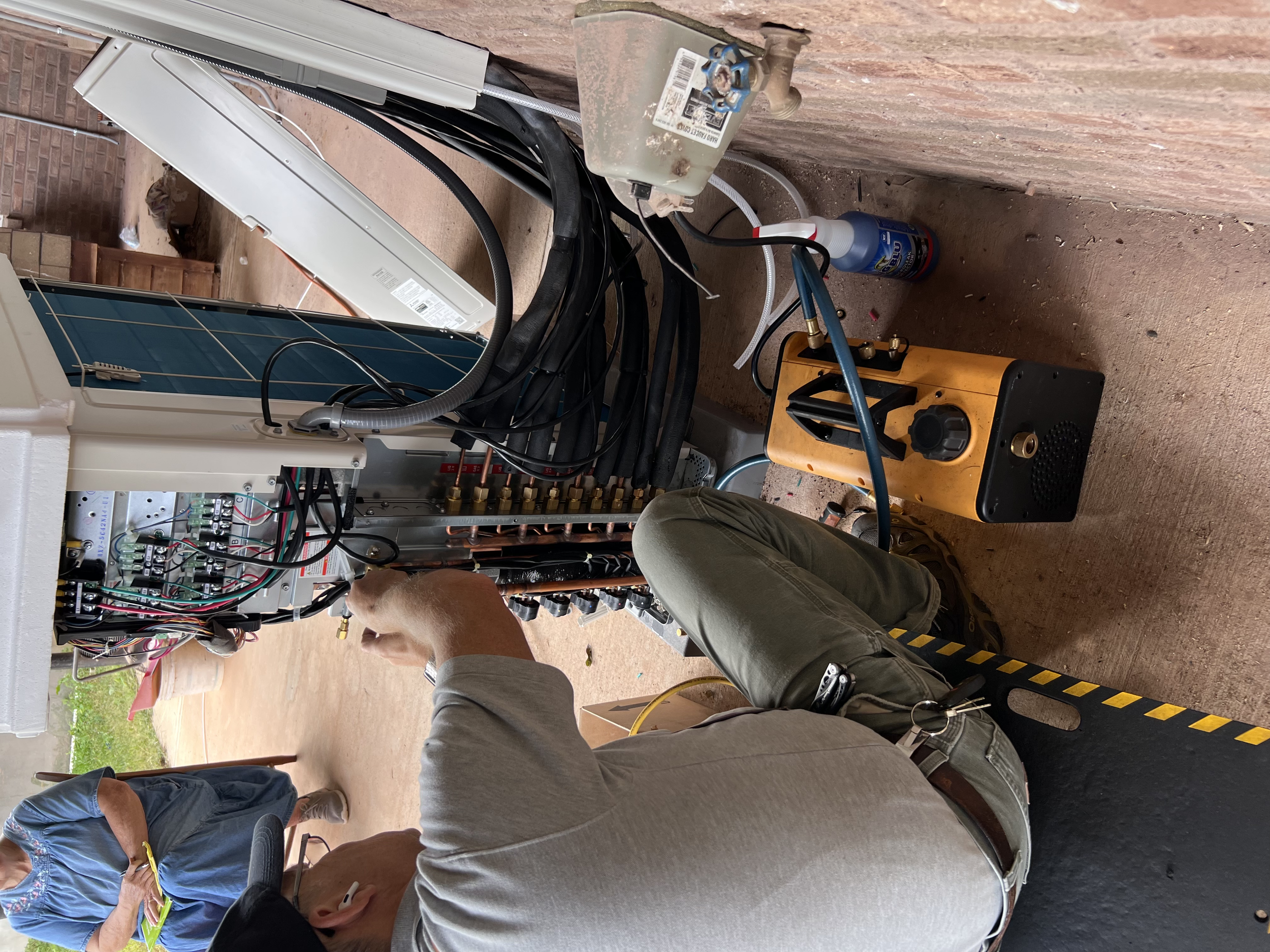 People working on electrical wiring inside a partially built structure with exposed brick walls and a concrete floor.