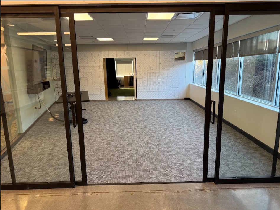 Empty office or conference room with large windows on the right, glass walls and door on the front, and a patterned wall on the back.