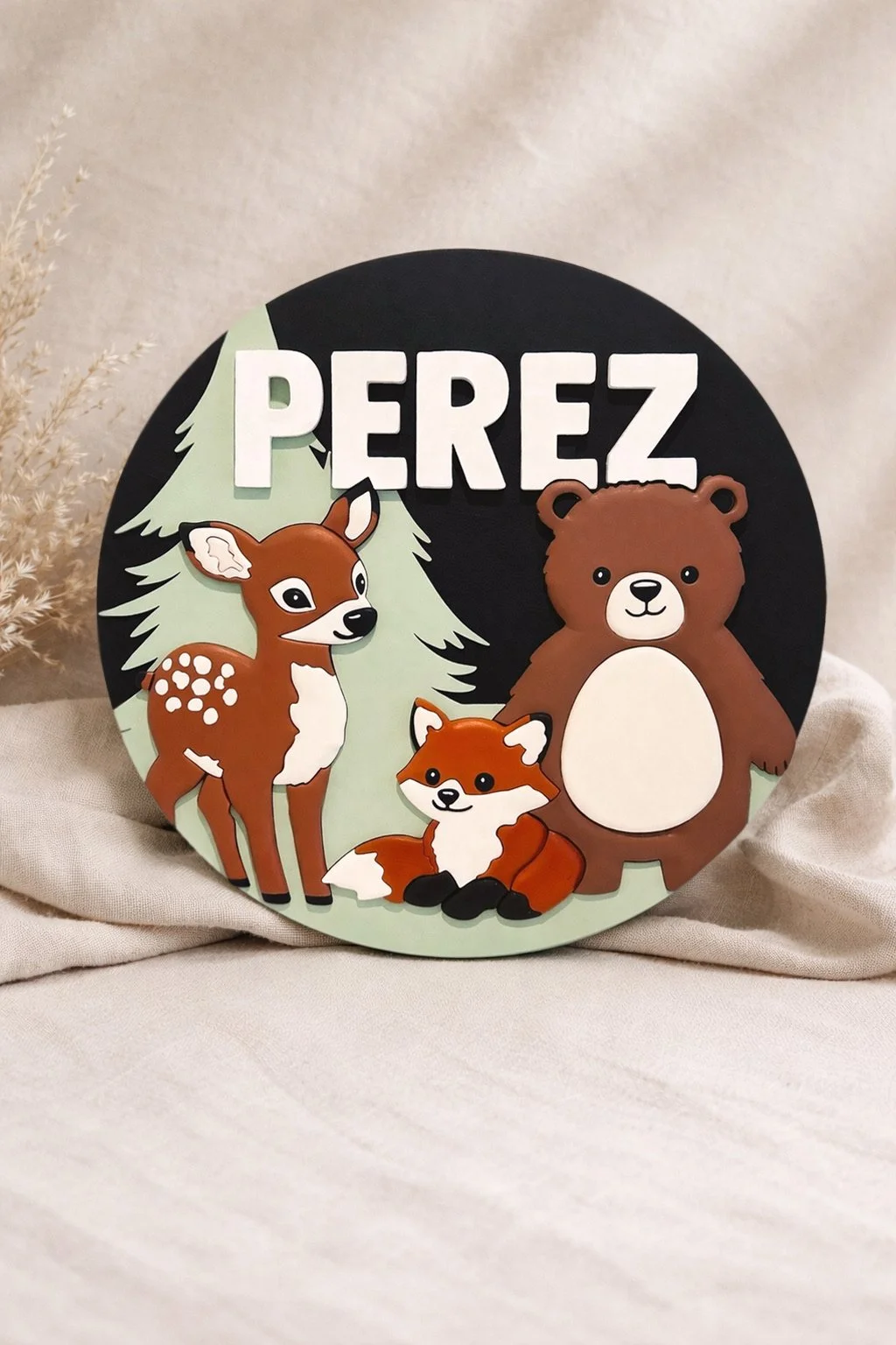 Round wooden name sign reading “PEREZ” with illustrated forest animals including a deer, bear, and fox in warm earthy colors.