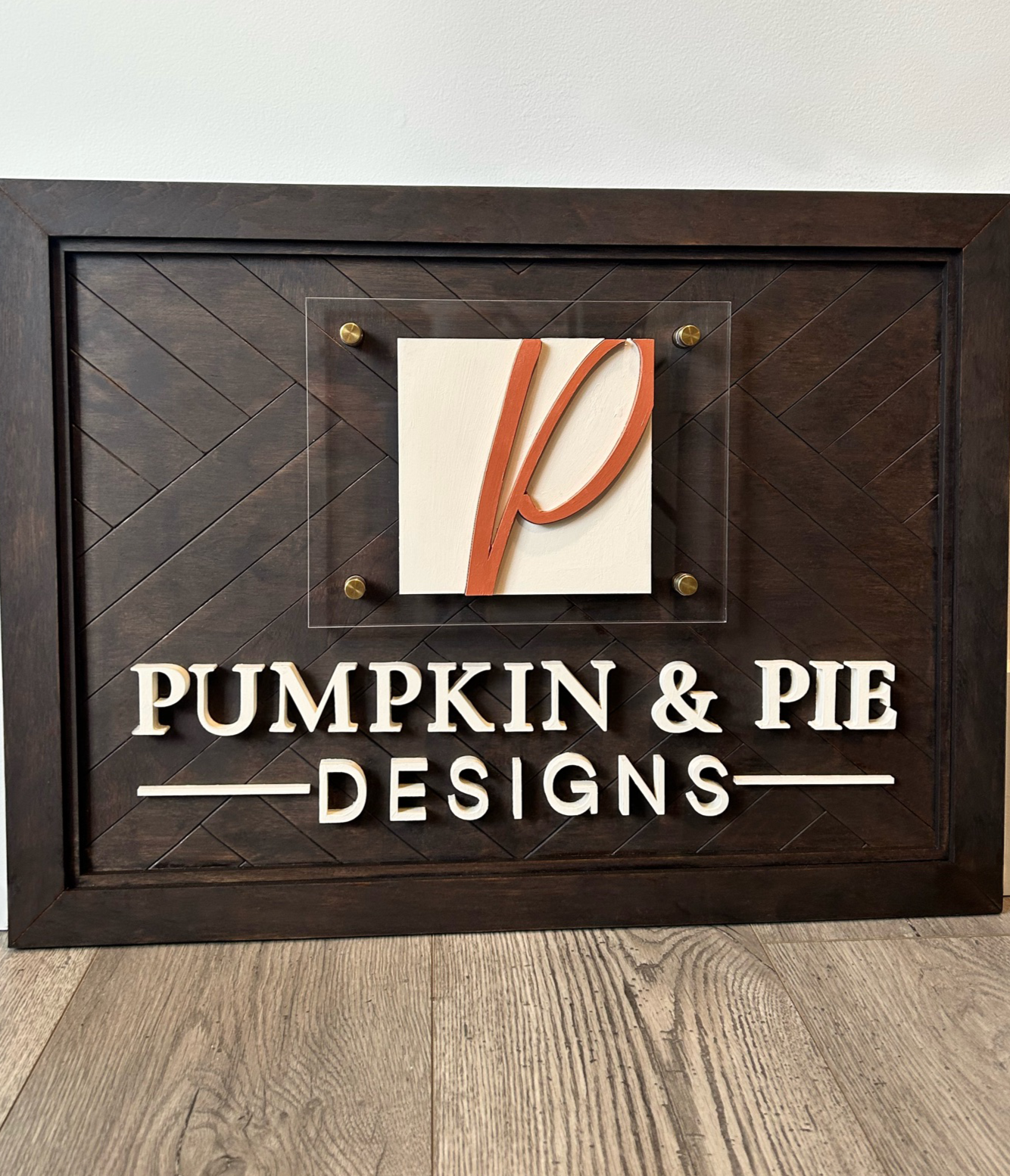 Modern layered sign featuring an abstract curved monogram in warm brown tones mounted on a white panel with acrylic framing.