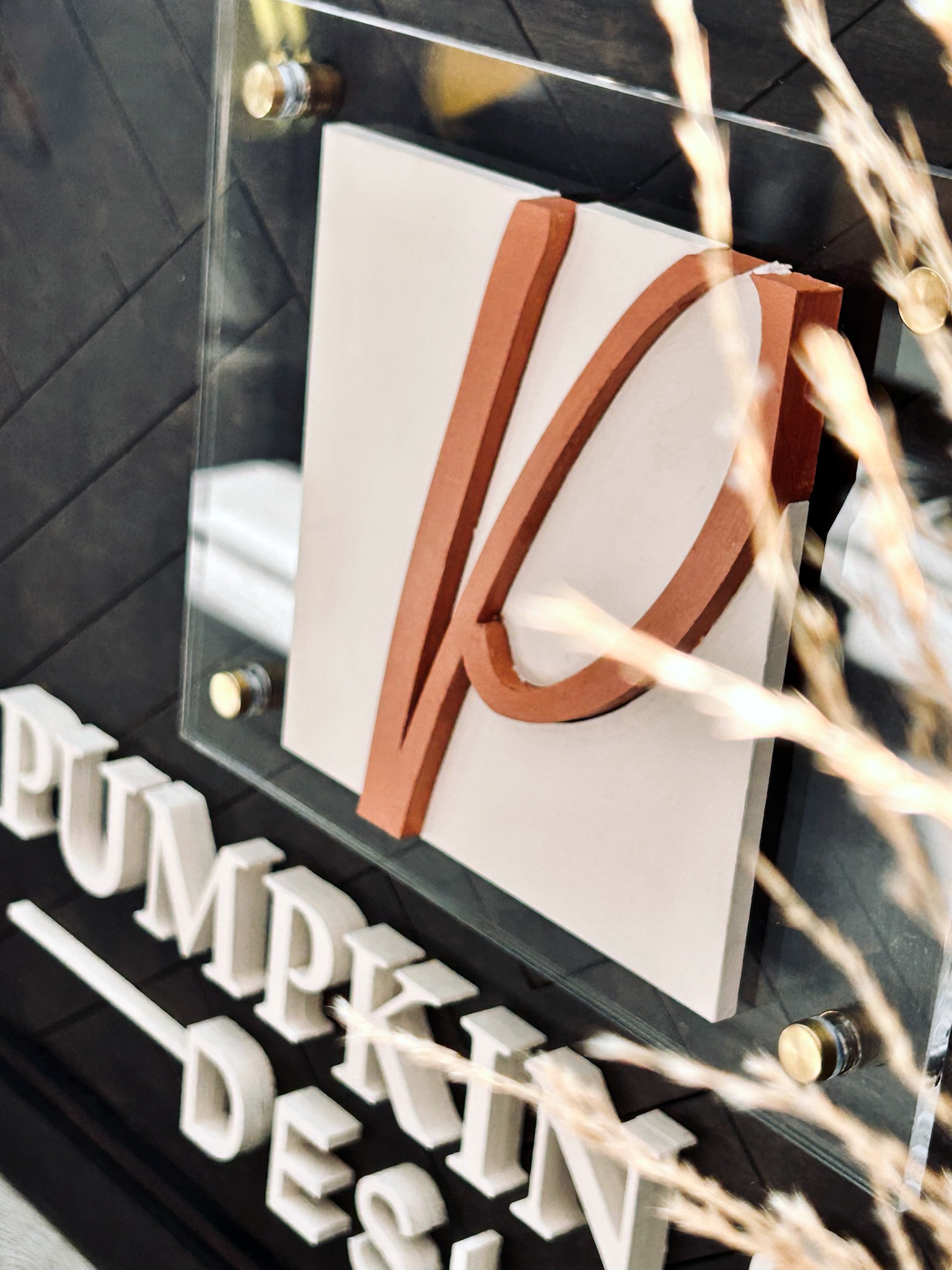 Modern layered sign featuring an abstract curved monogram in warm brown tones mounted on a white panel with acrylic framing.