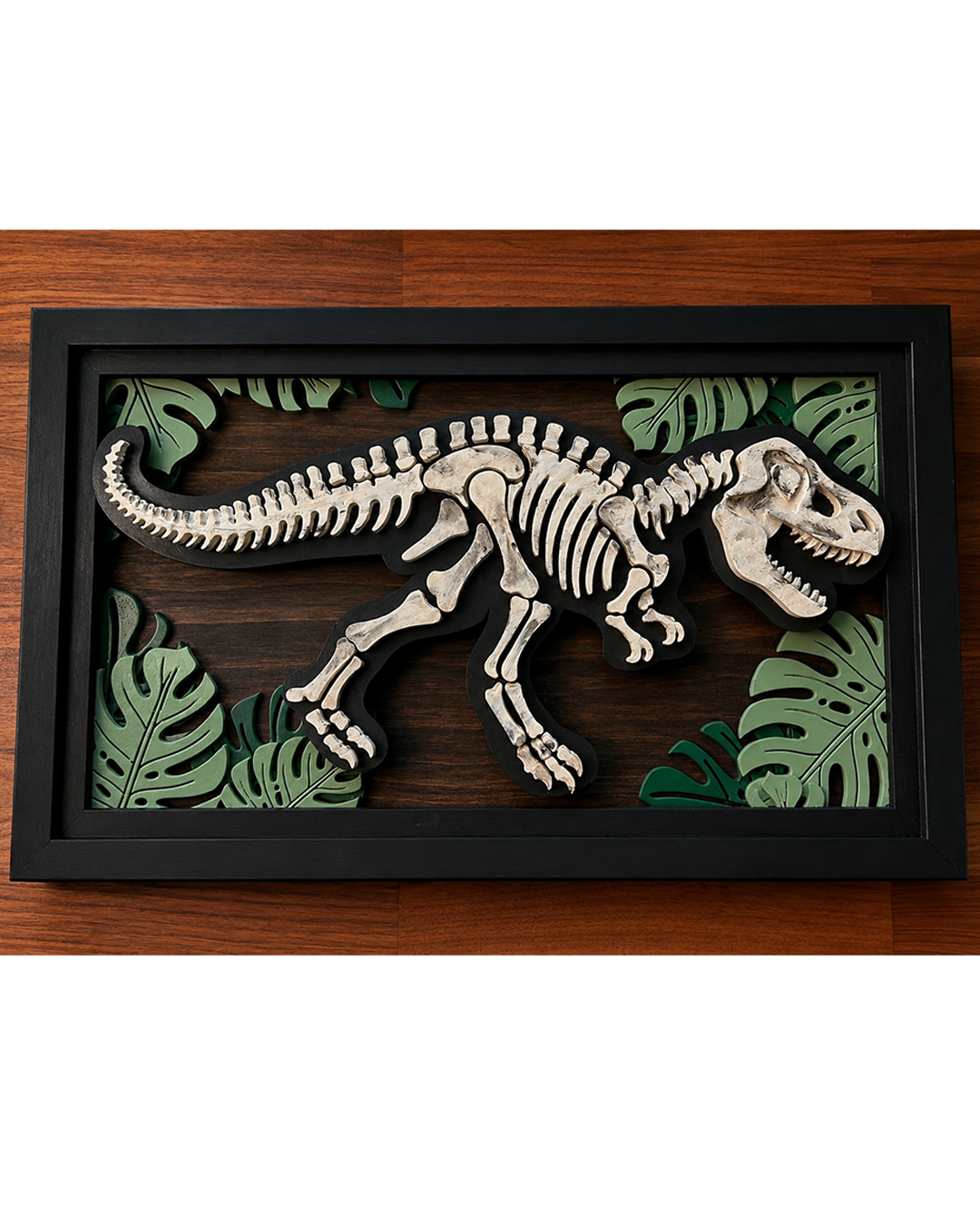 Layered wooden dinosaur skeleton wall art with tropical leaf accents and black frame.
