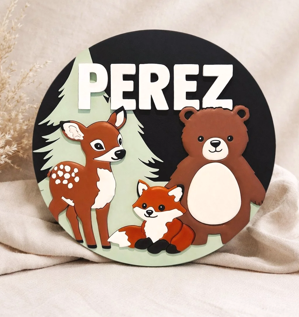 Round wooden name sign reading “PEREZ” with illustrated forest animals including a deer, bear, and fox in warm earthy colors.