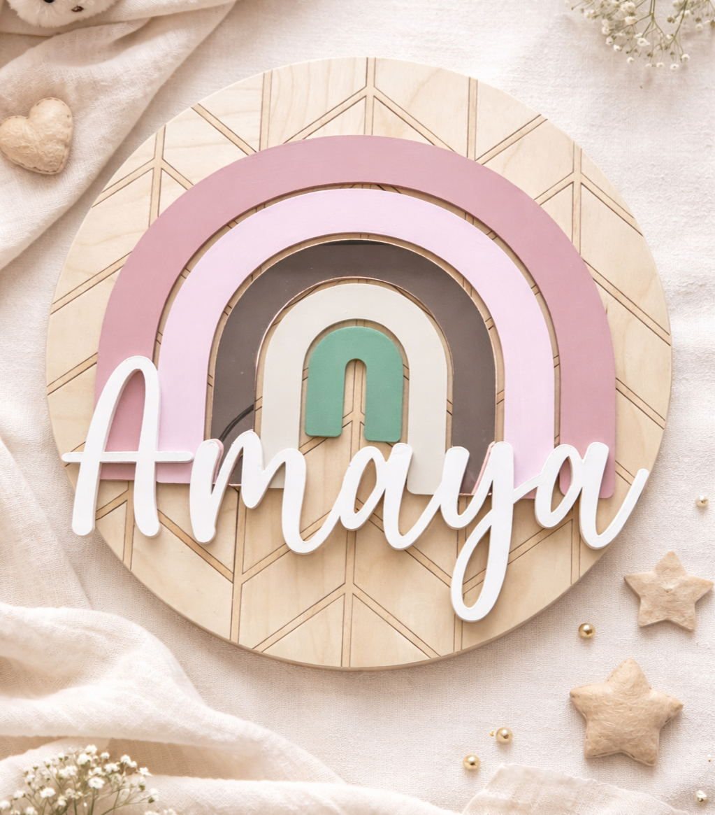 Layered wooden name sign reading “Amaya” with a pastel rainbow and geometric background in soft pink, tan, and green tones.