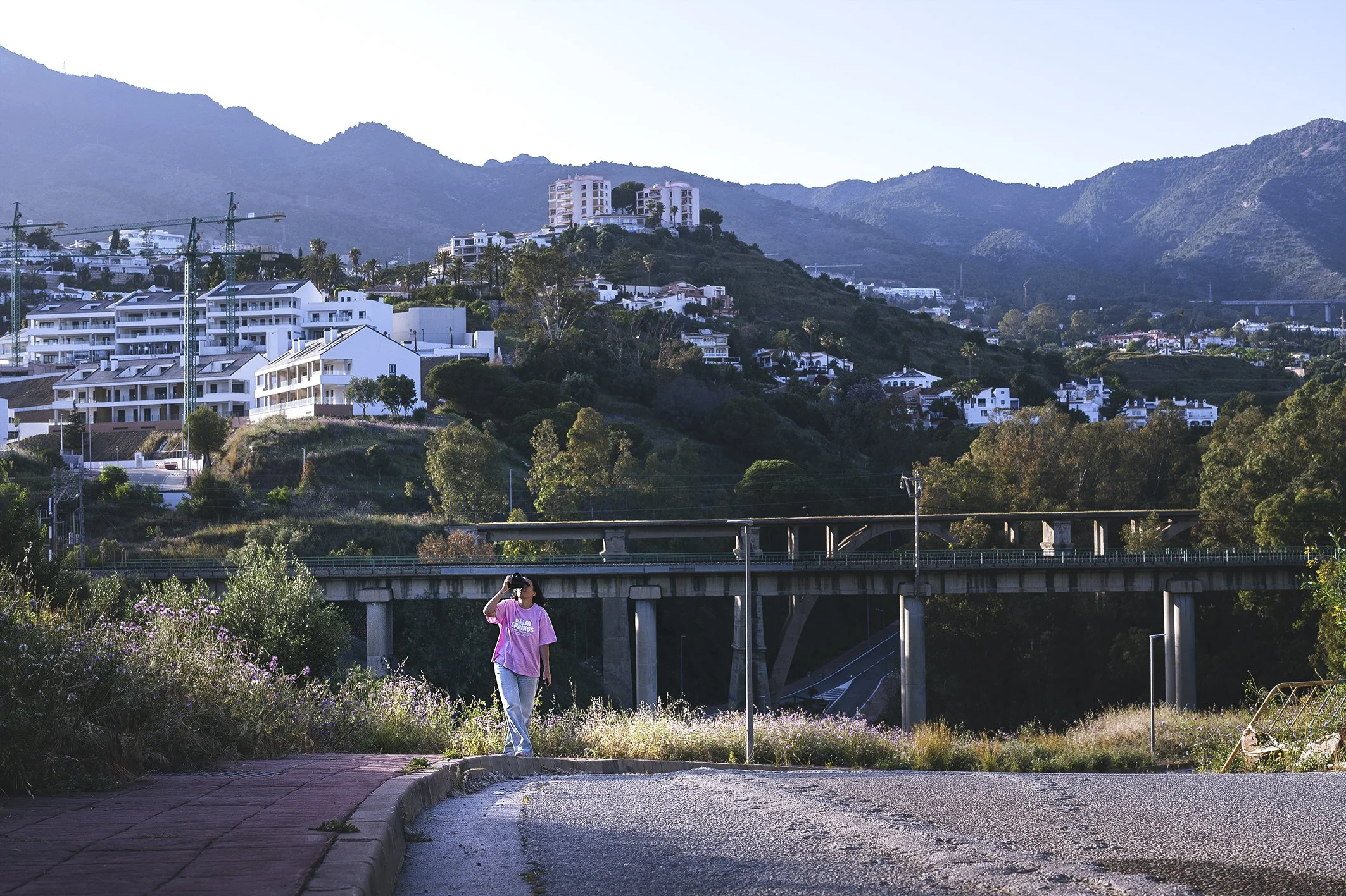 una fotografa profesional caminando por Benalmadena, sacando fotos, vestida de jean clarito y camiseta rosa, y por supuesta, su cámara profesional Nikon