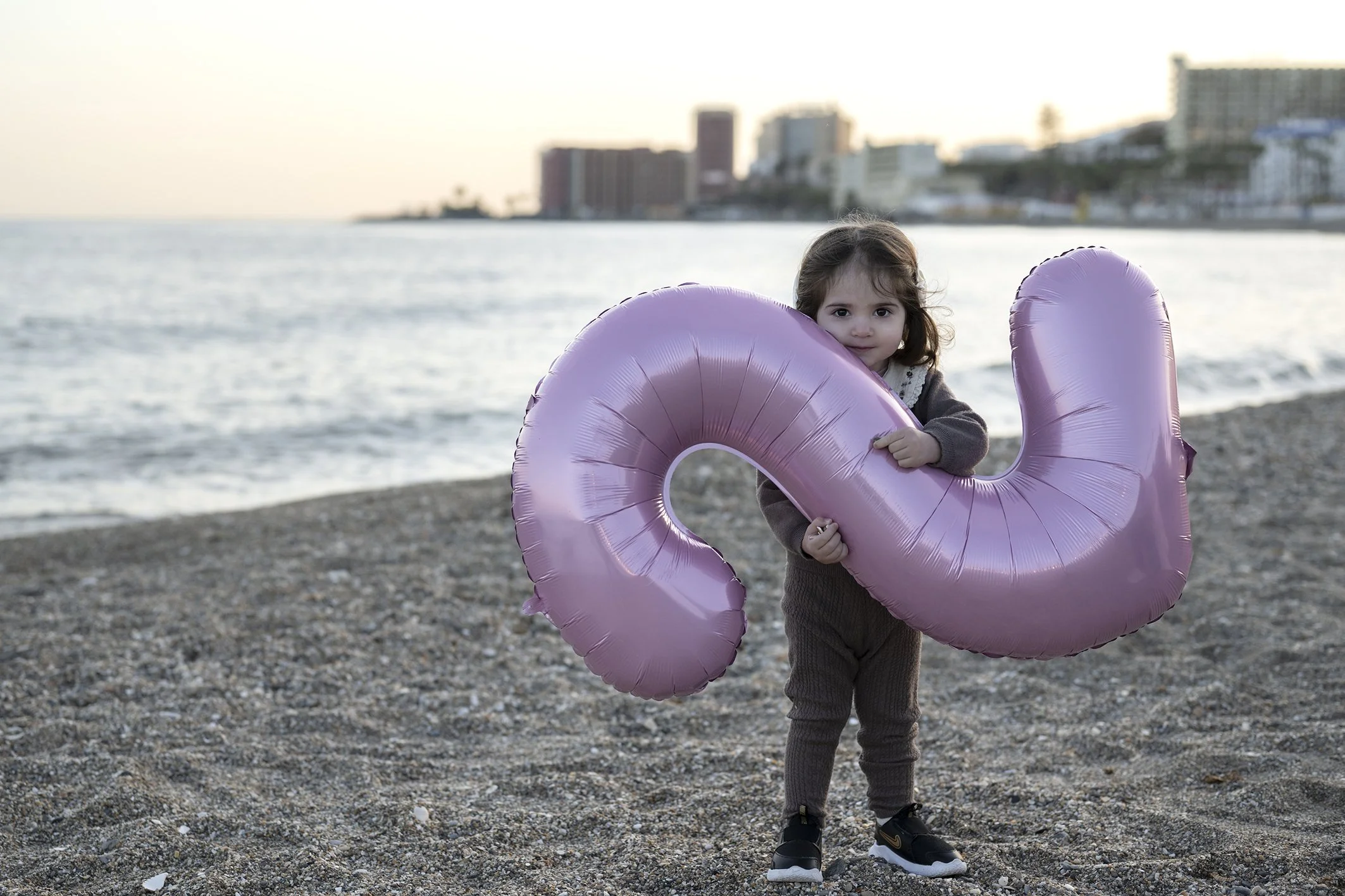 niña festejando su cumpleaños numero 2 con un globo rosa mientras le hacen fotos en la playa en Benalmádena 