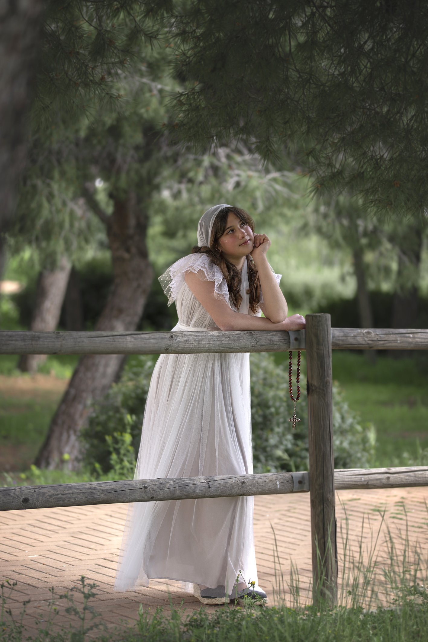 Una niña pensativa con un rosario vestida de comunión en un bosque en Benalmádena 