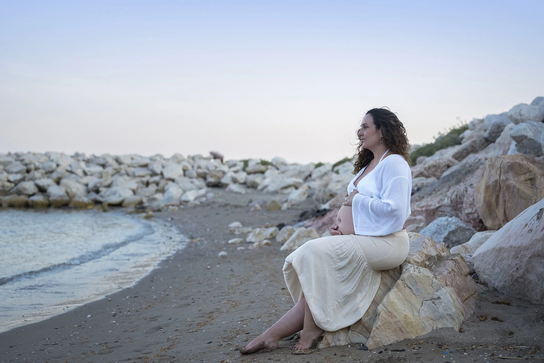Mujer sonriendo mirando el mar mientras hace un reportaje fotográfico de embarazo en la playa en Benalmádena 