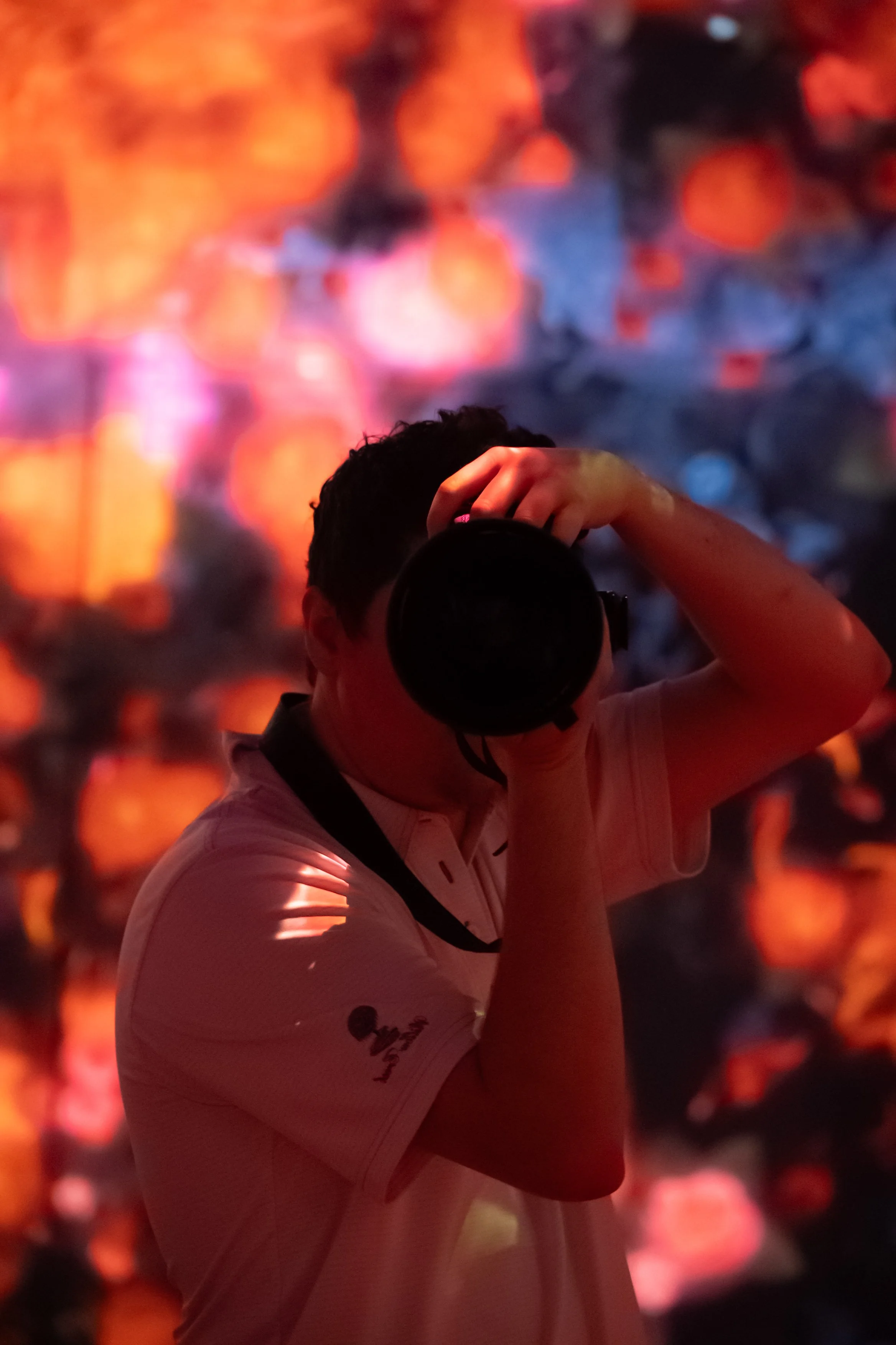 Person taking a photo with a camera in front of a colorful, out-of-focus background of red, orange, and blue hues.