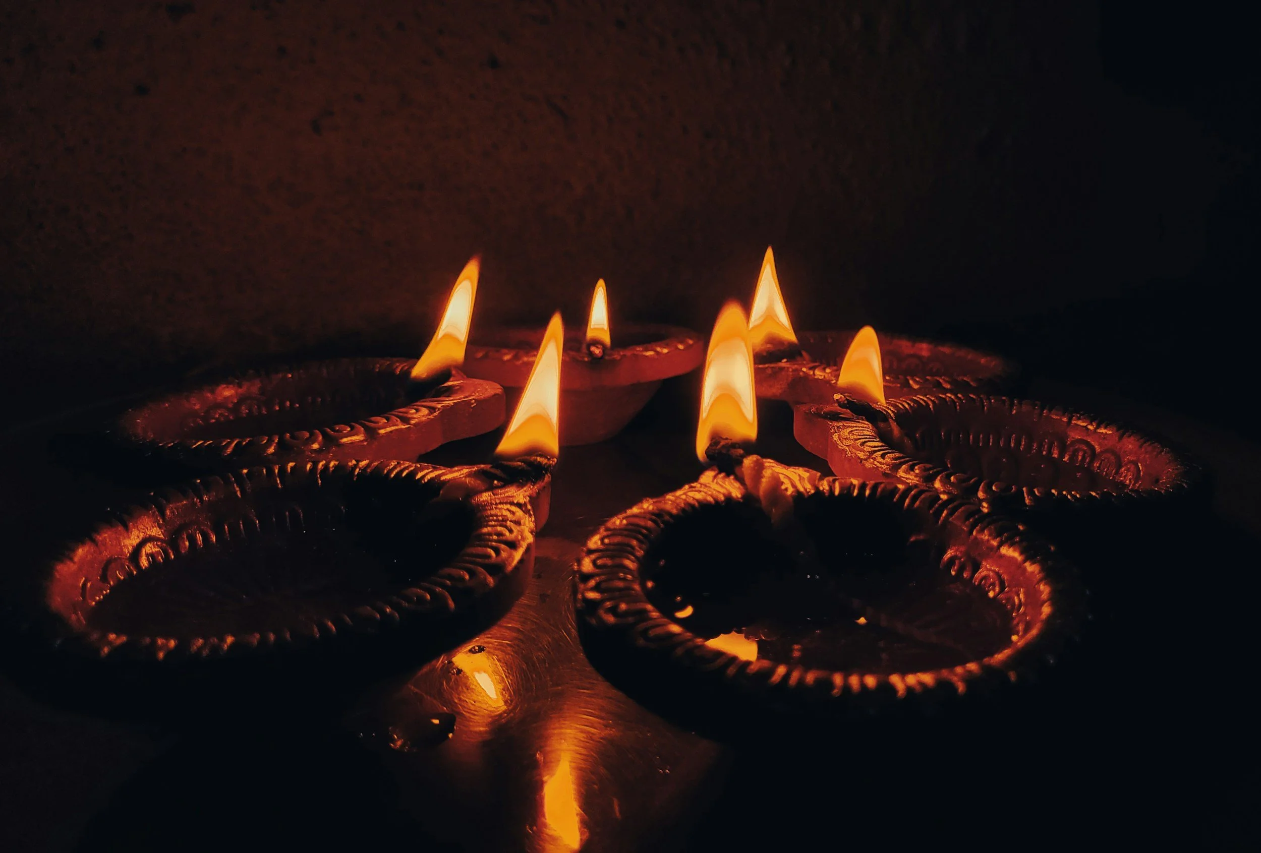 Diwali lamps (diyas) lit with flames, arranged on a dark surface.