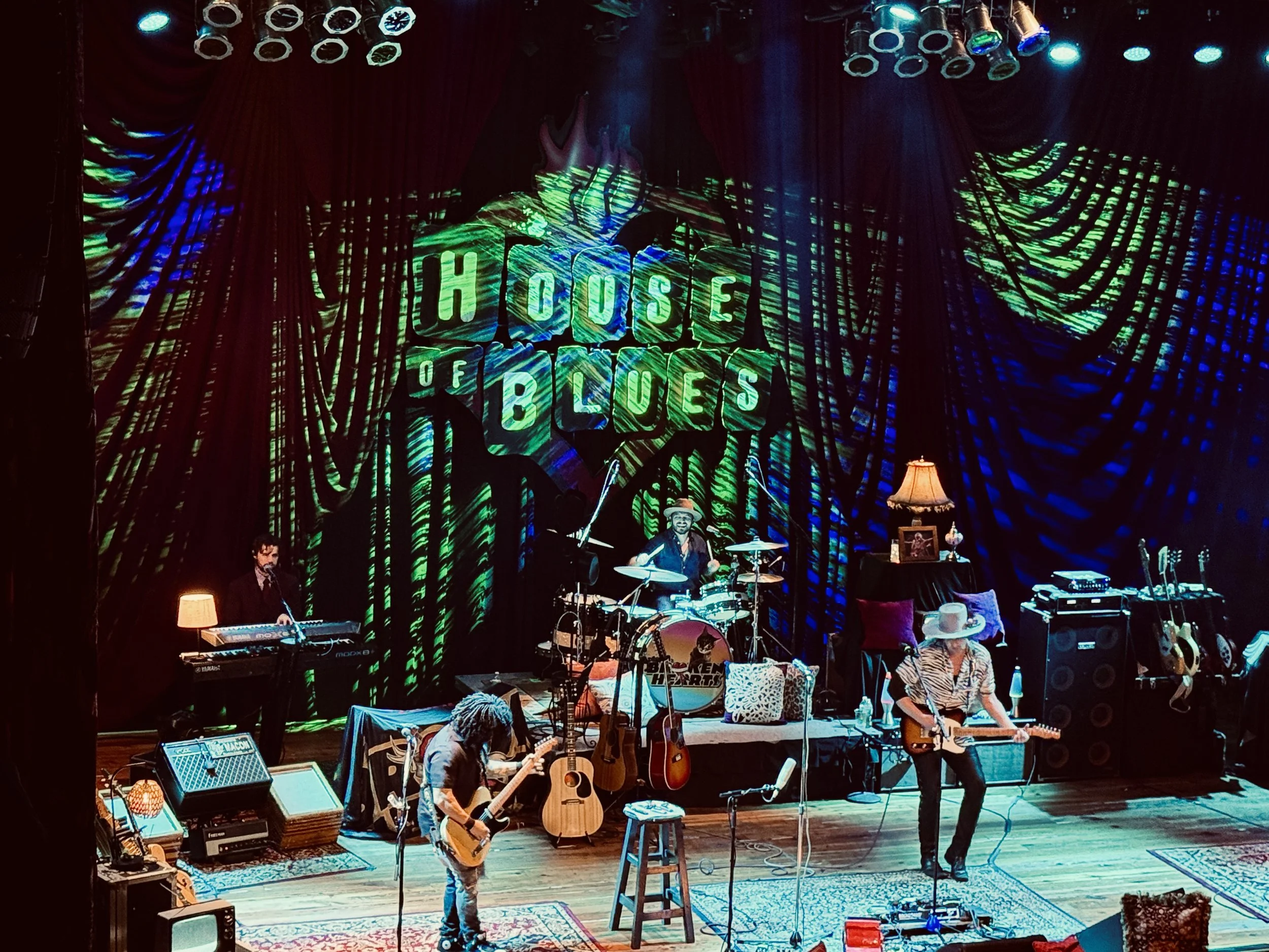 Musicians performing on stage with a colorful backdrop reading 'House of Blues'. The band includes a keyboard player, drummer, and guitarist with a hat, surrounded by guitars and stage equipment. Chrome Horse: The Bob Dylan Tribute. Myrtle Beach, SC