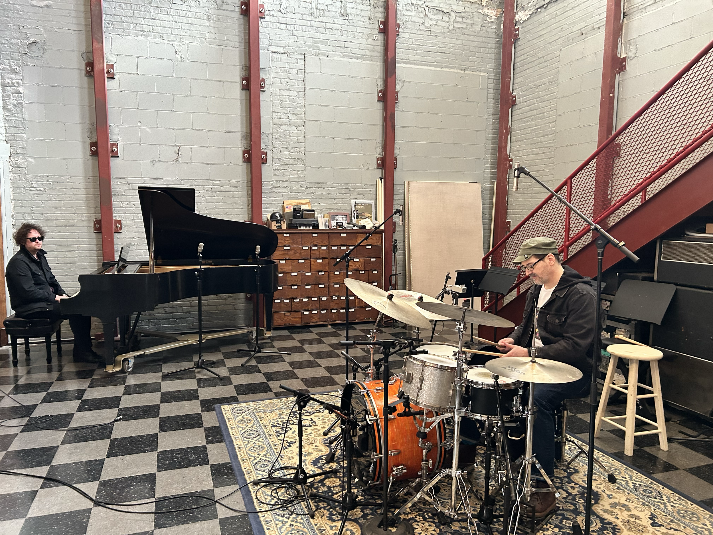 A musician playing drums and another playing piano in a studio with brick walls and a checkered floor. at Electrical Audio, Chicago, IL