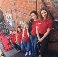 Group of young women in red shirts lined up on stairs against a brick wall