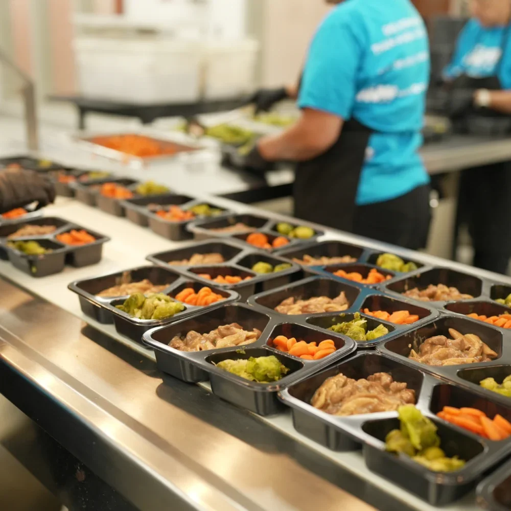 Multiple meal trays with chicken, carrots, and green beans on a serving counter in a cafeteria or kitchen setting.
