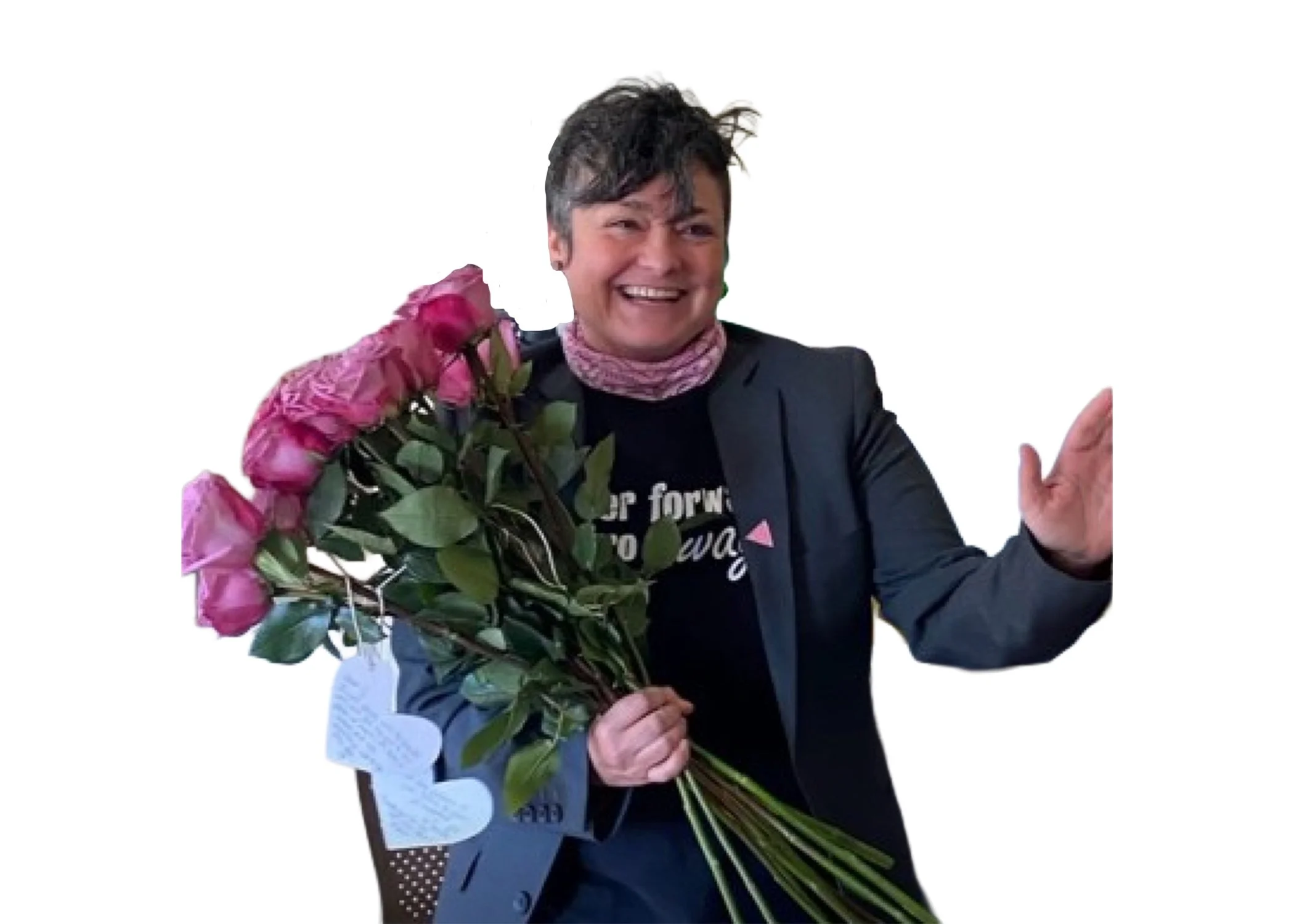 Person with dark hair smiling, holding a bouquet of pink roses, wearing a black jacket and a black shirt with text, standing against a plain white background.