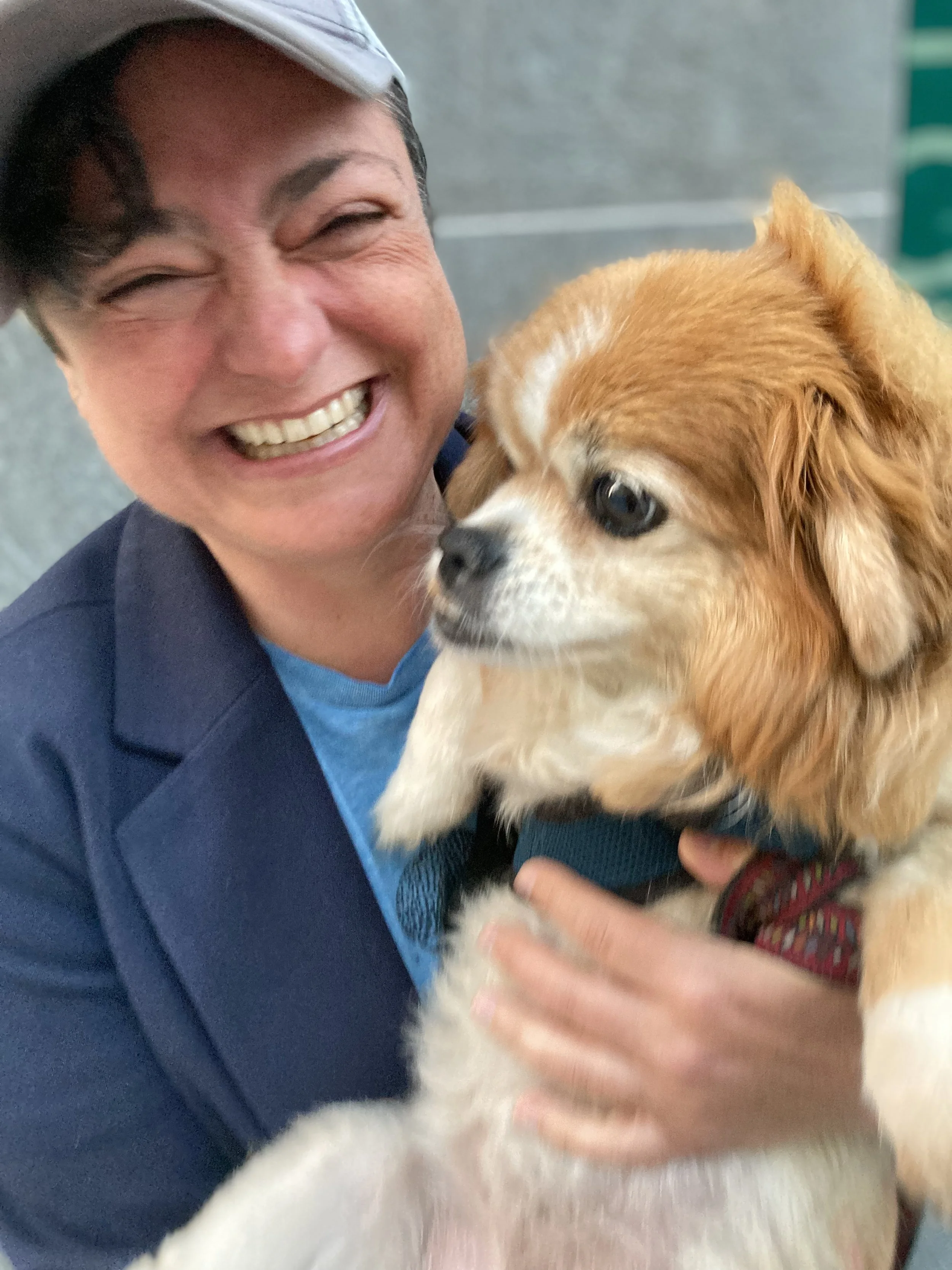 Jesse Rose Cohen, LCSW, an online therapist in California smiling broadly while holding a small tan and white dog with long ears and a black harness.