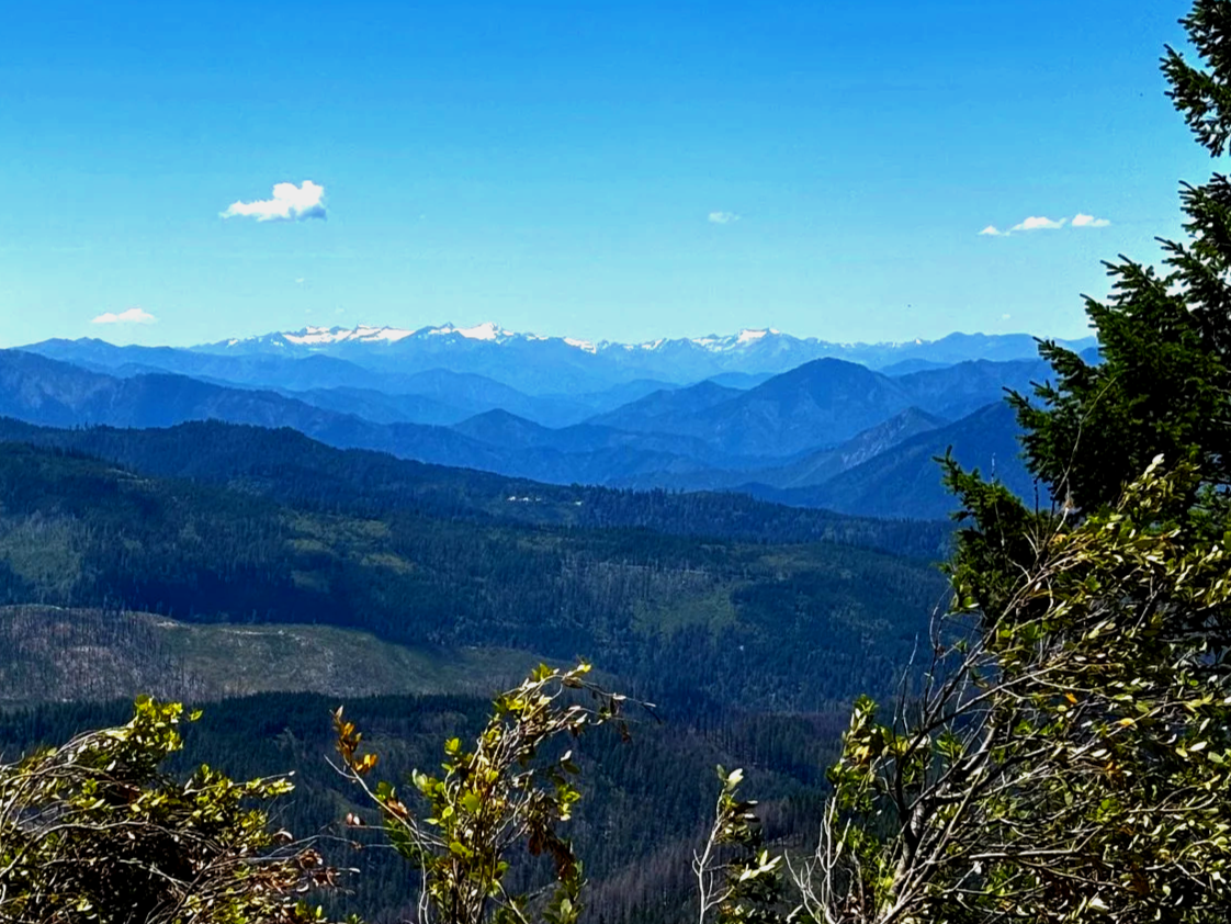 Scenic view of multiple mountain ranges with snow-capped peaks in the distance under a blue sky with a few scattered clouds.