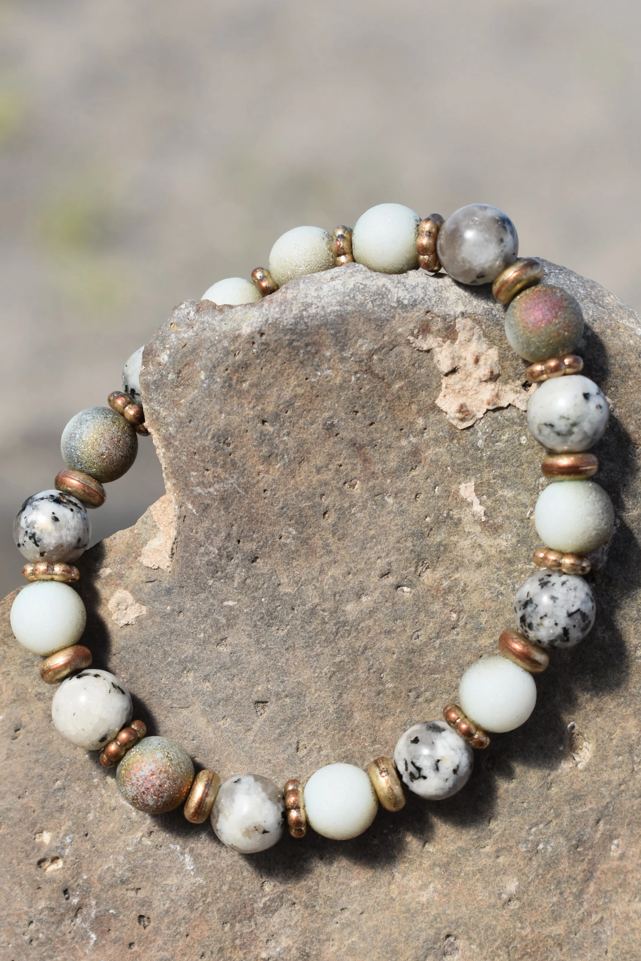 Beaded bracelet with various colored round beads resting on a rough stone.
