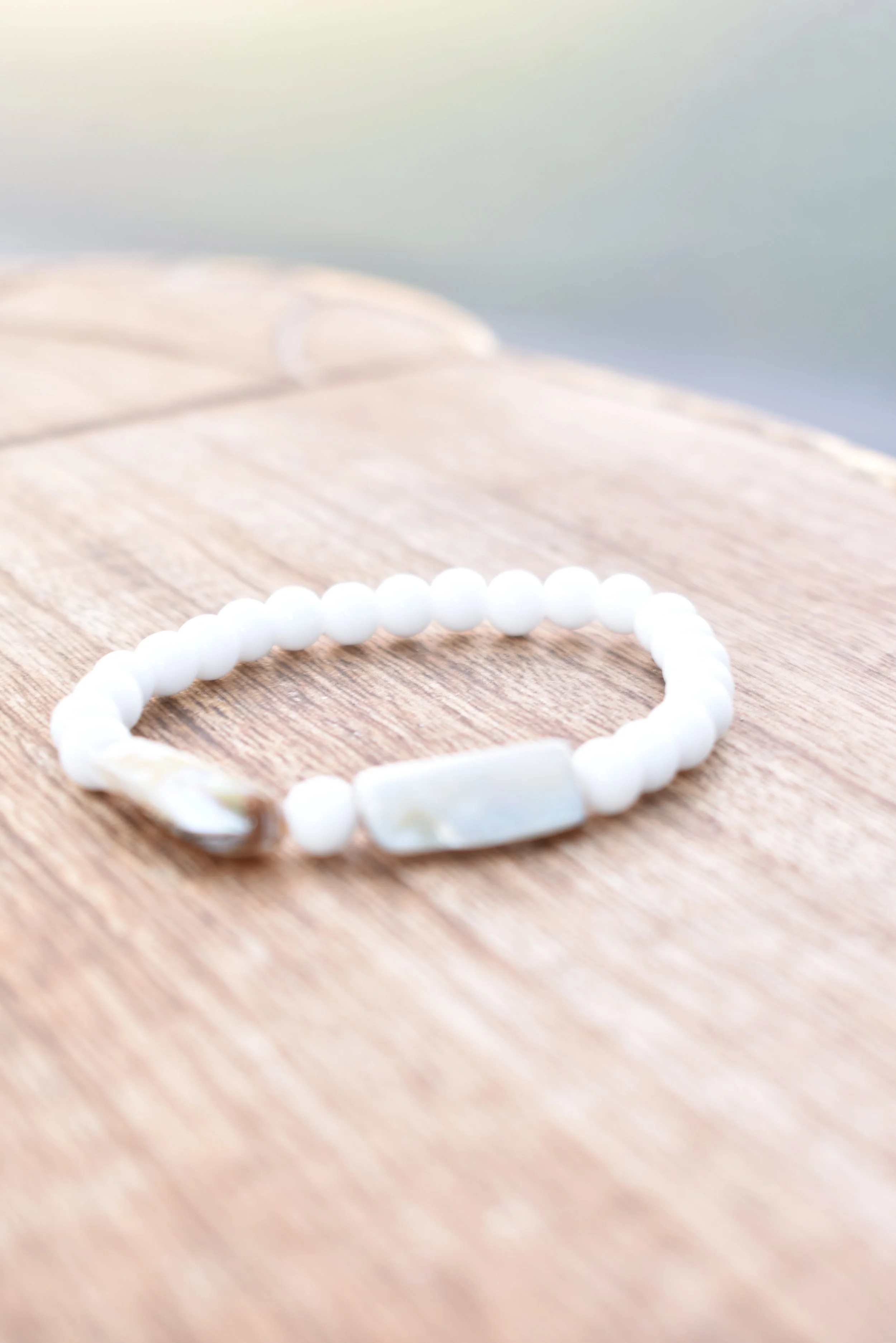 A white beaded bracelet with a rectangular central bead resting on a wooden surface.