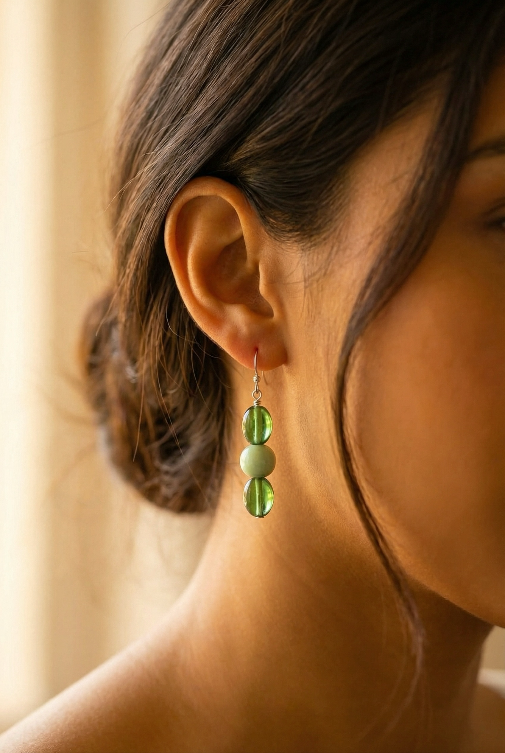 Close-up of a woman's ear wearing a dangle earring with green and white beads.
