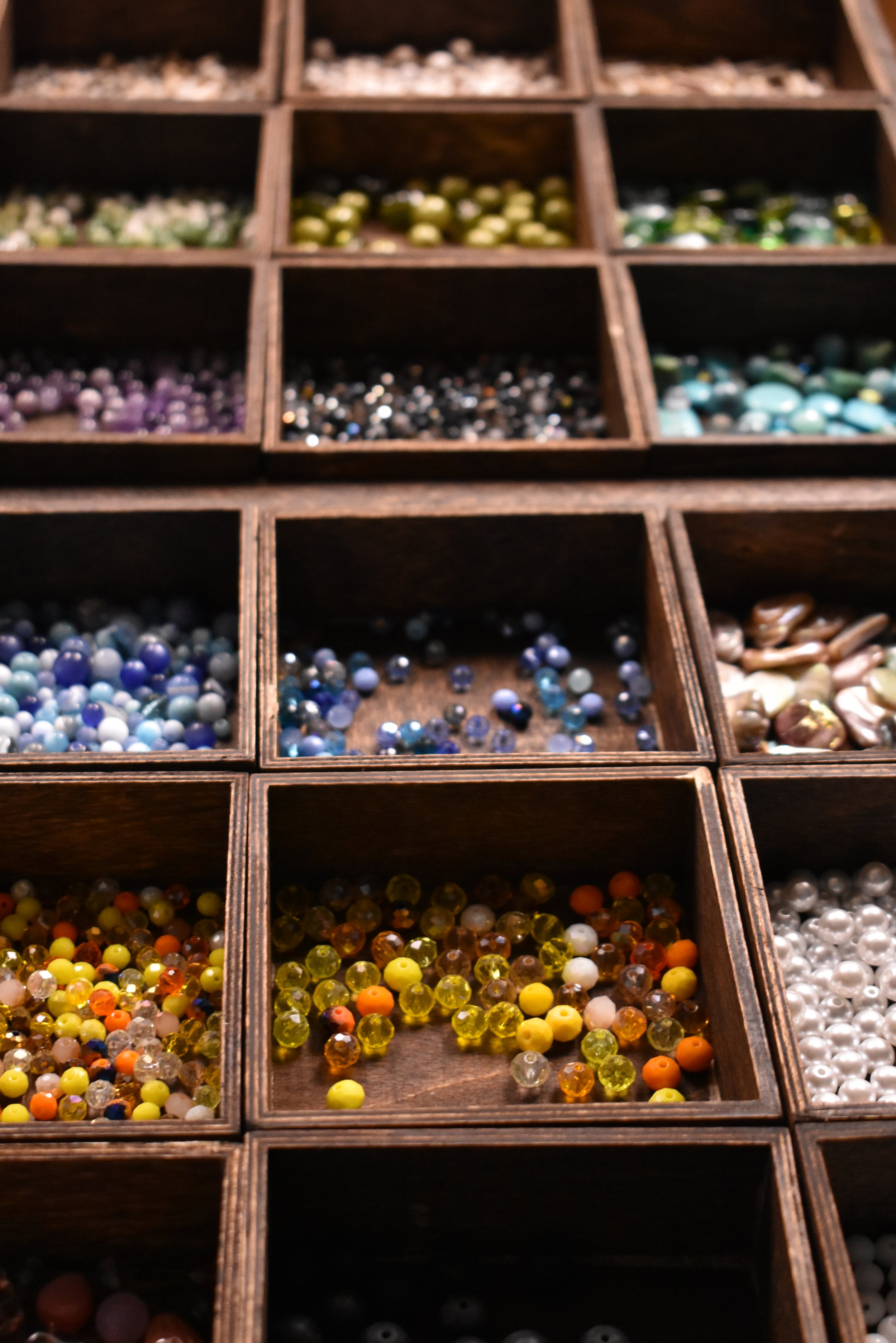 A wooden box with multiple compartments, each containing colorful beads in various sizes and shades.