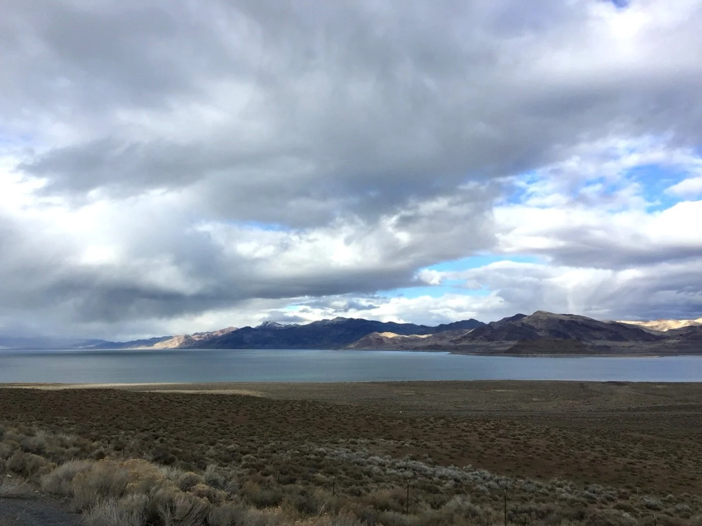 A landscape view showing a large body of water with mountains in the background under a cloudy sky.