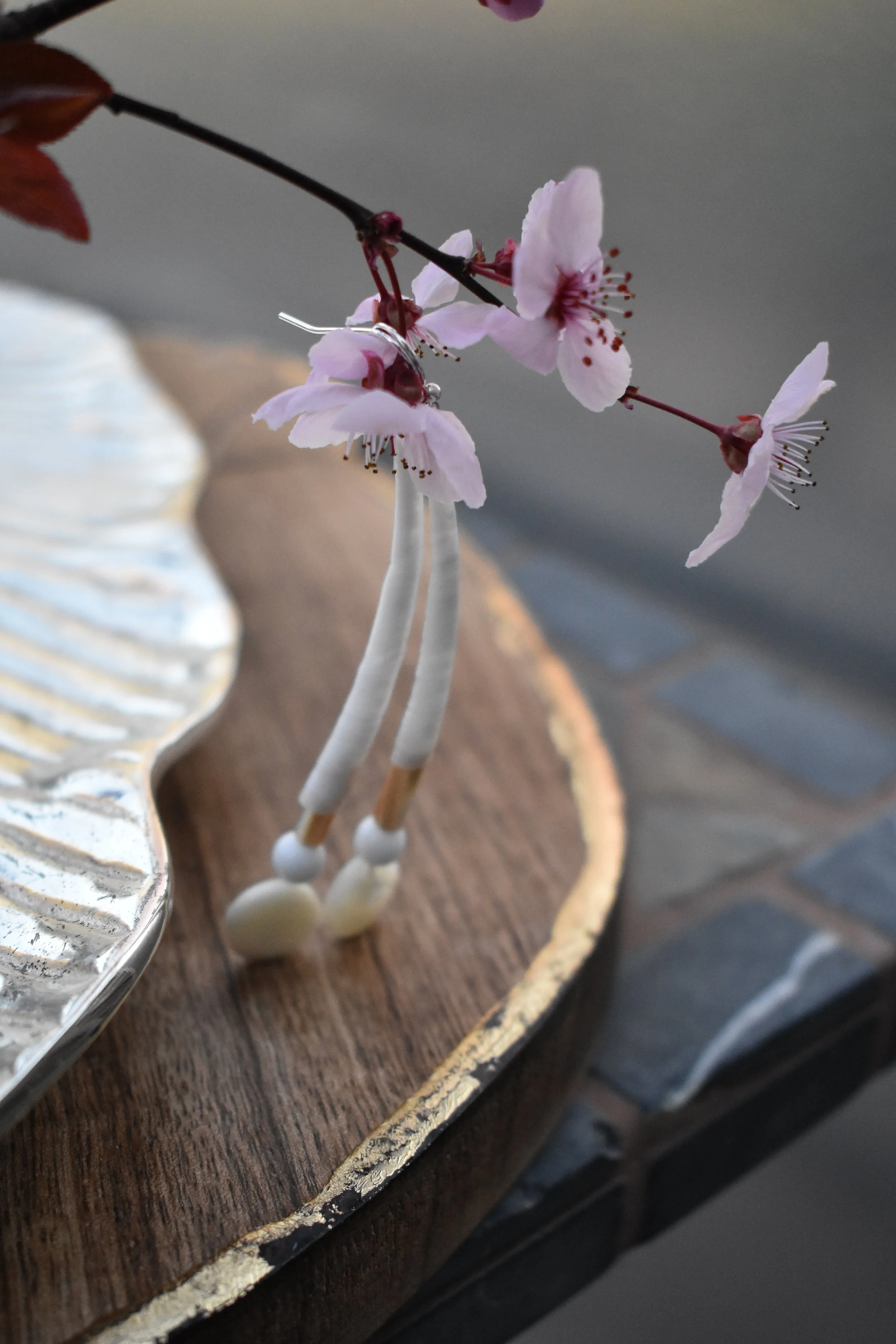 Close-up of pink cherry blossoms on a branch, with a wooden and metal decorative tray and a brick surface in the background.