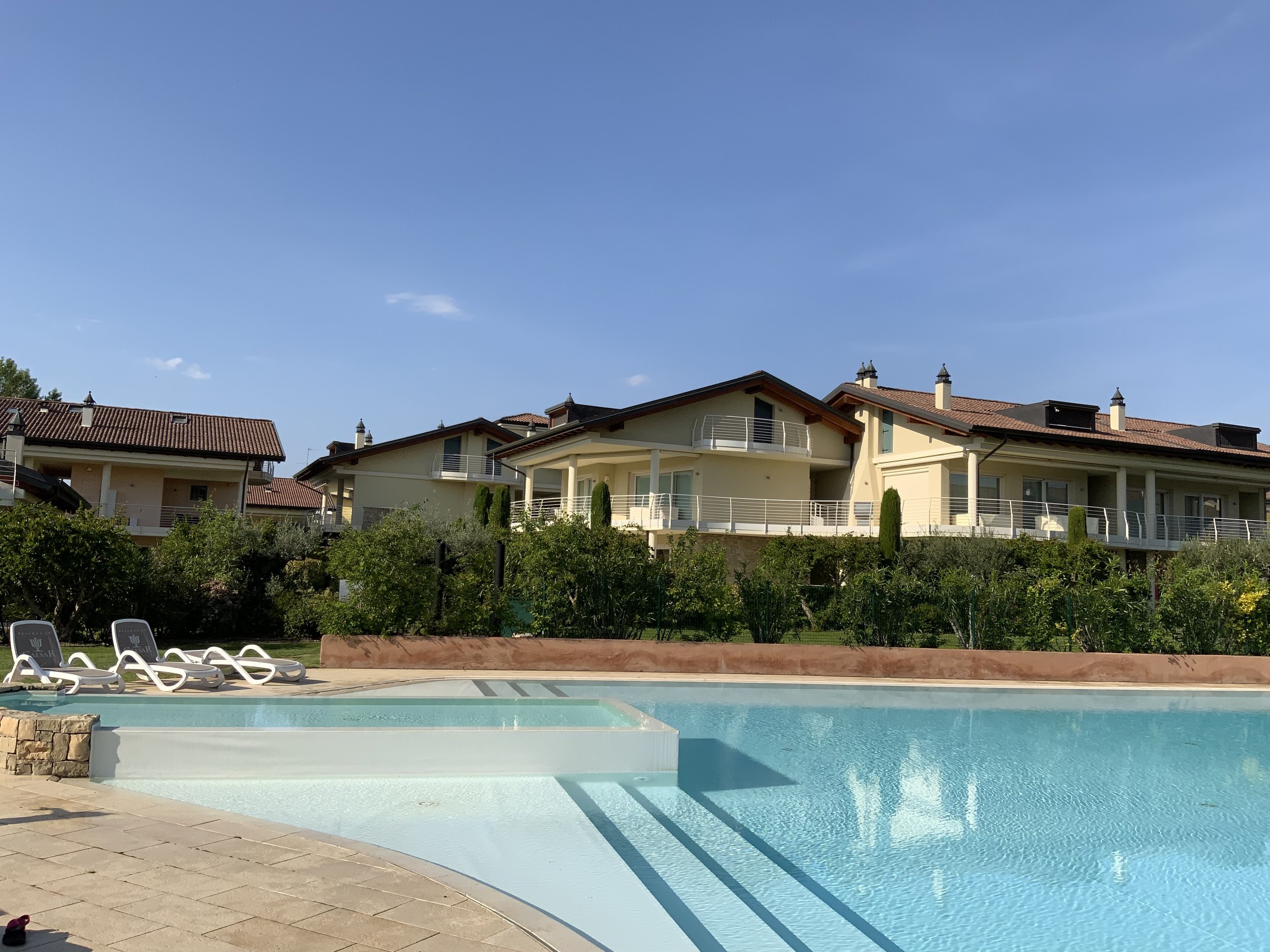 Luxury residential houses with a swimming pool in the foreground, green garden, clear blue sky, on a sunny day.