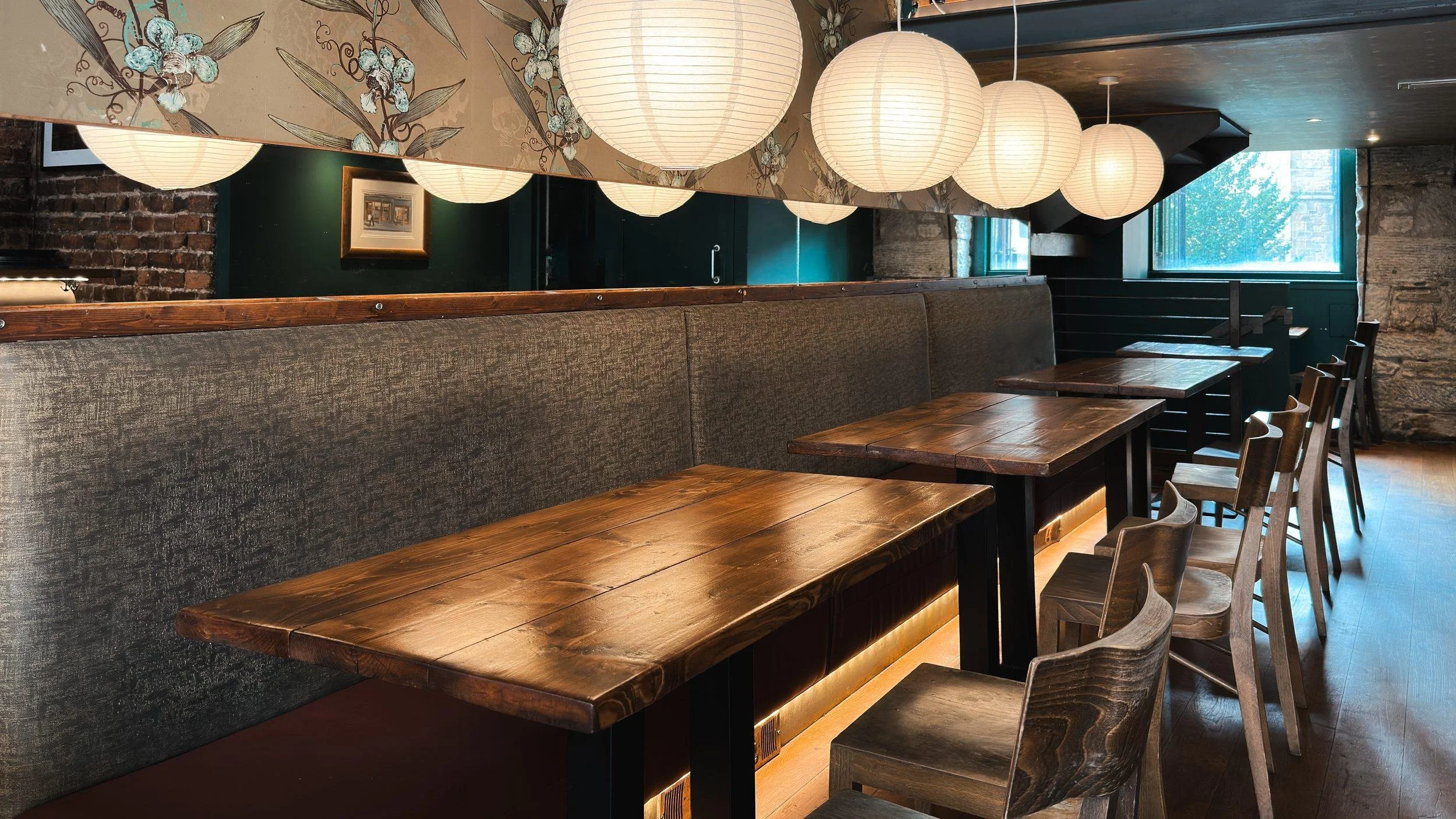 A long banquette with wooden tables under paper lanterns at The Left Bank.