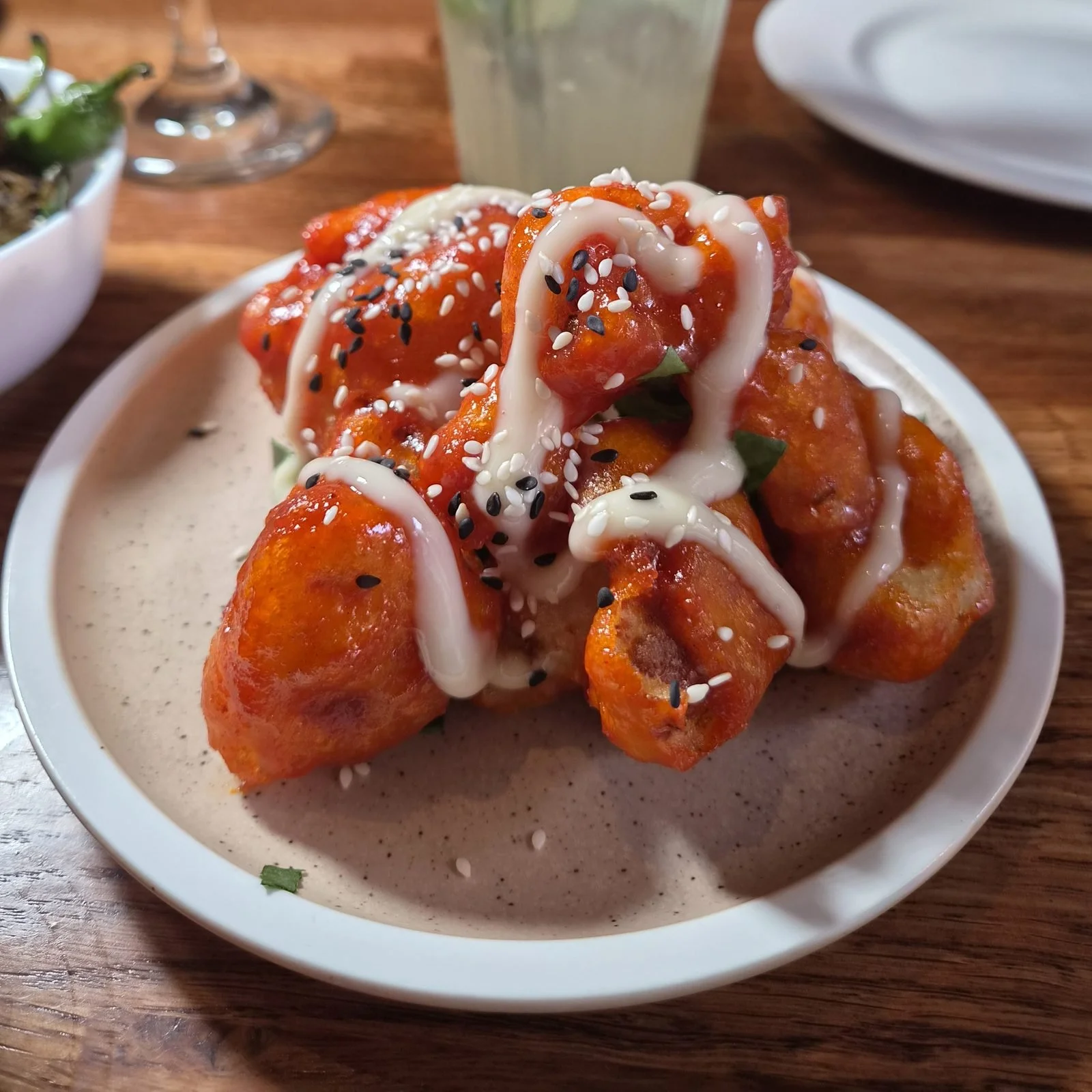 Korean cauliflower with kewpie mayo and sesame seeds at The Left Bank, with a cocktail and padron peppers on the table behind.