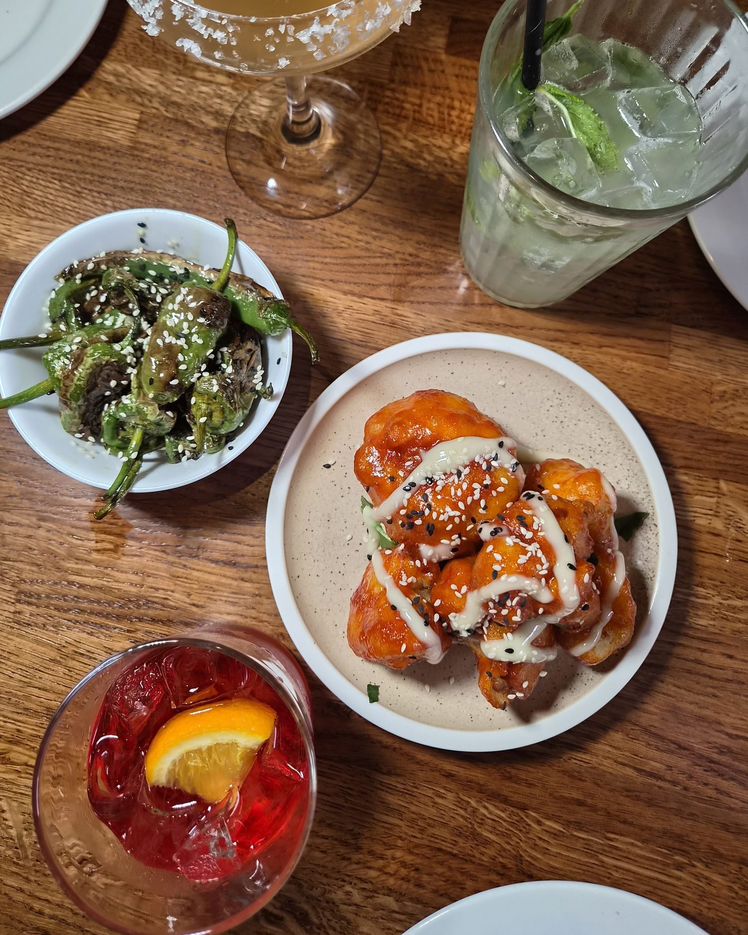 Plates to share at The Left Bank: Korean cauliflower and padron peppers with a margarita, a mojito and a negroni on a wooden table.