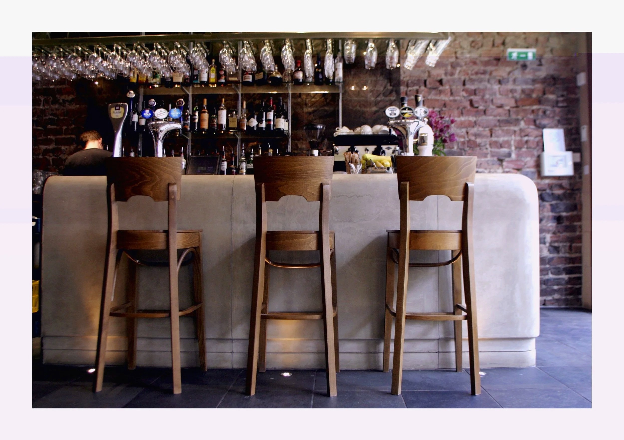 Wooden stools at the stone bar of The Left Bank, Gibson Street, Glasgow, with glassware and bottles behind