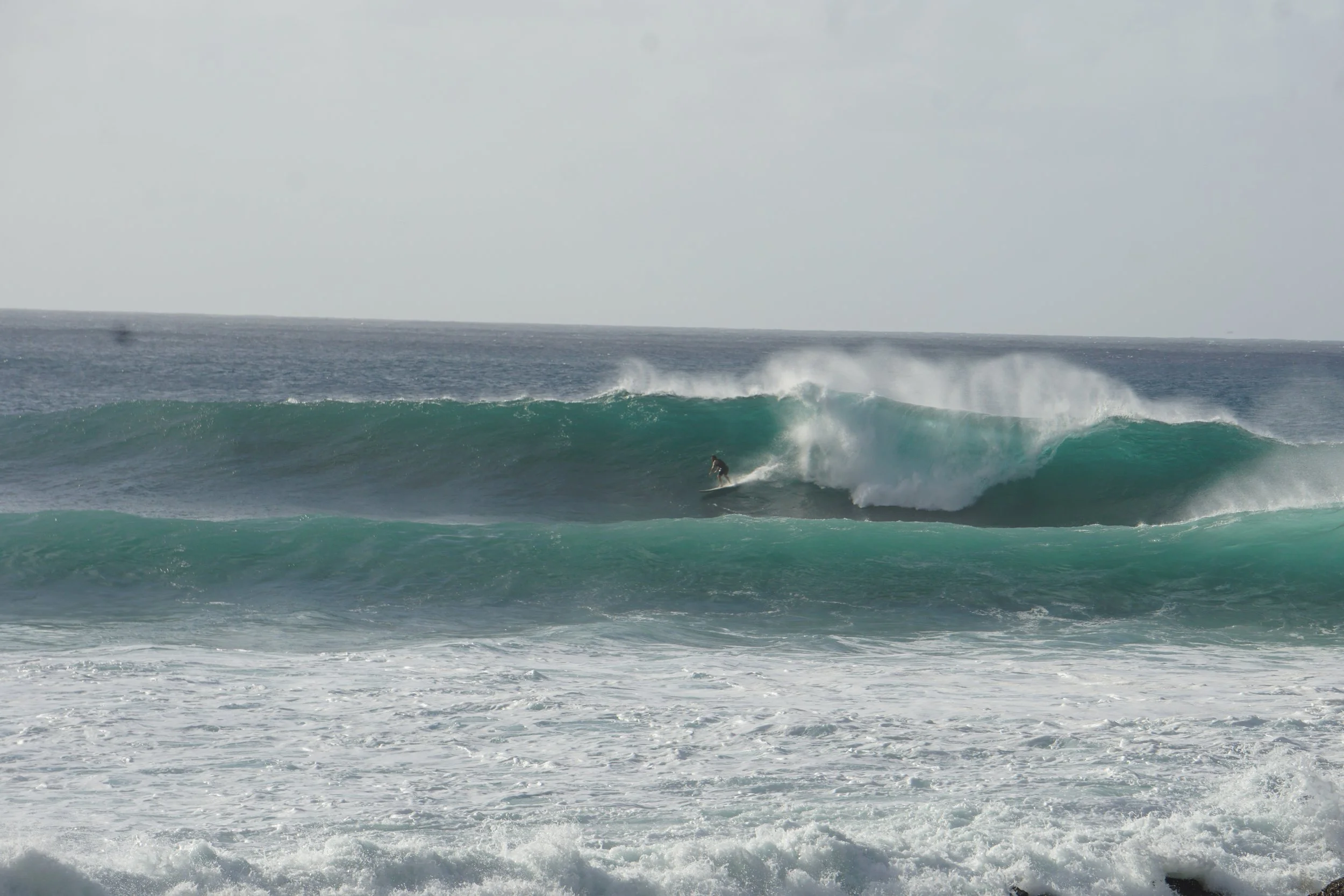 A founder of smokin pigeon riding a large wave in costa rica with white spray and foam.