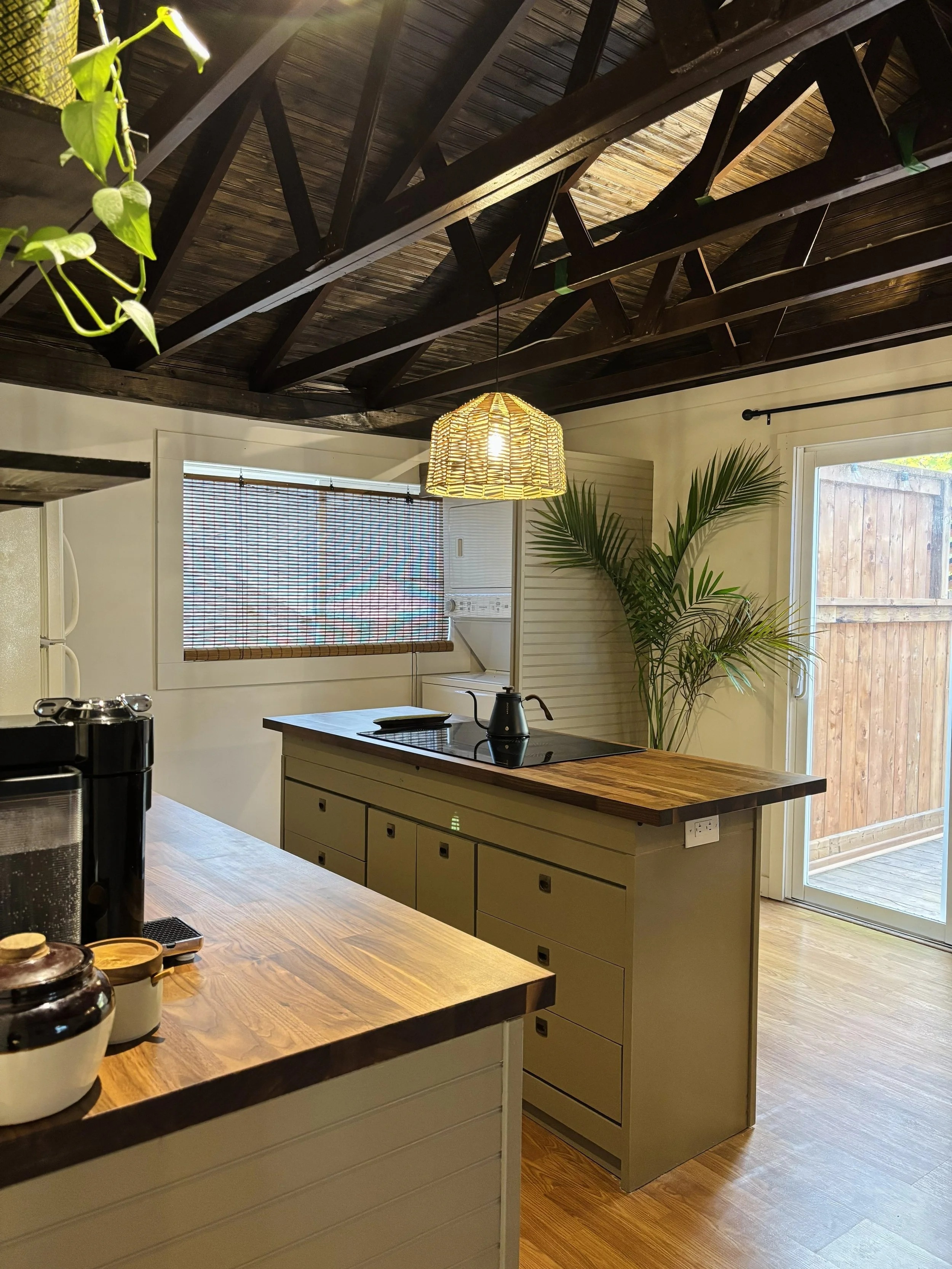 Kitchen with wooden countertops, a large window with a bamboo blind, a potted plant, and a wooden ceiling with exposed dark beams.