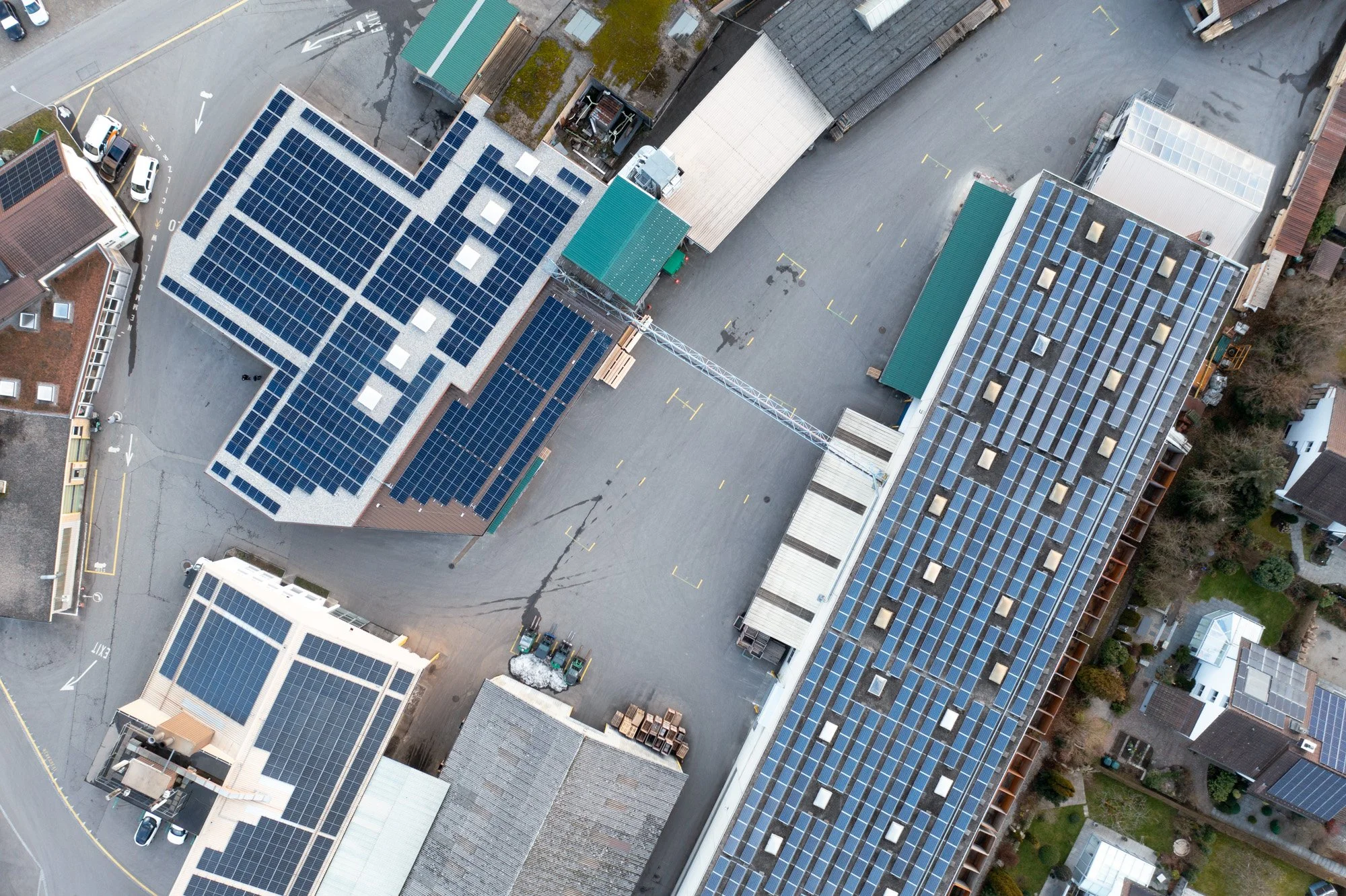 Aerial view of multiple rooftops with solar panels installed, surrounding a paved parking lot and nearby streets.
