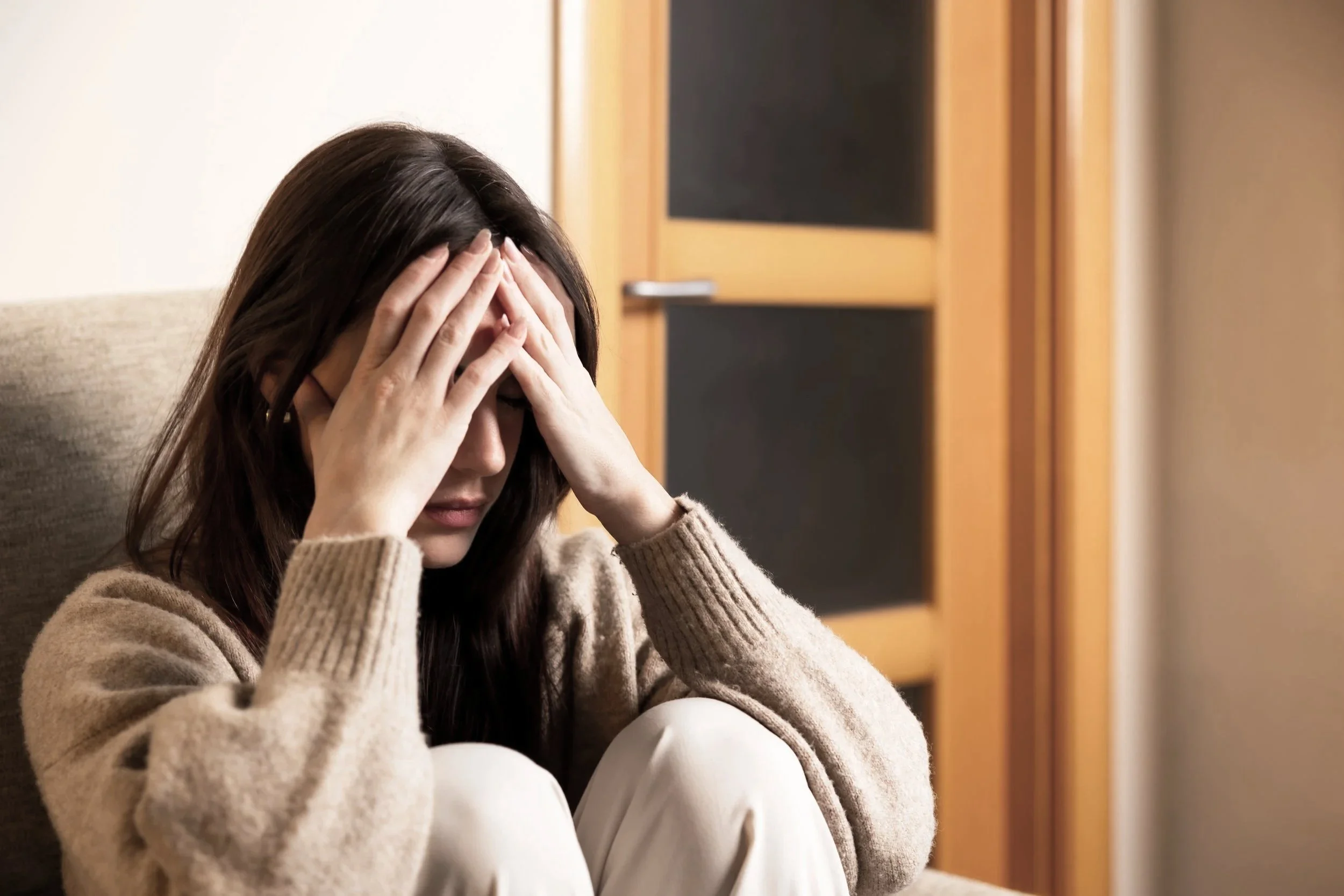 A woman sitting on a couch with her hands on her forehead, appearing distressed or upset.